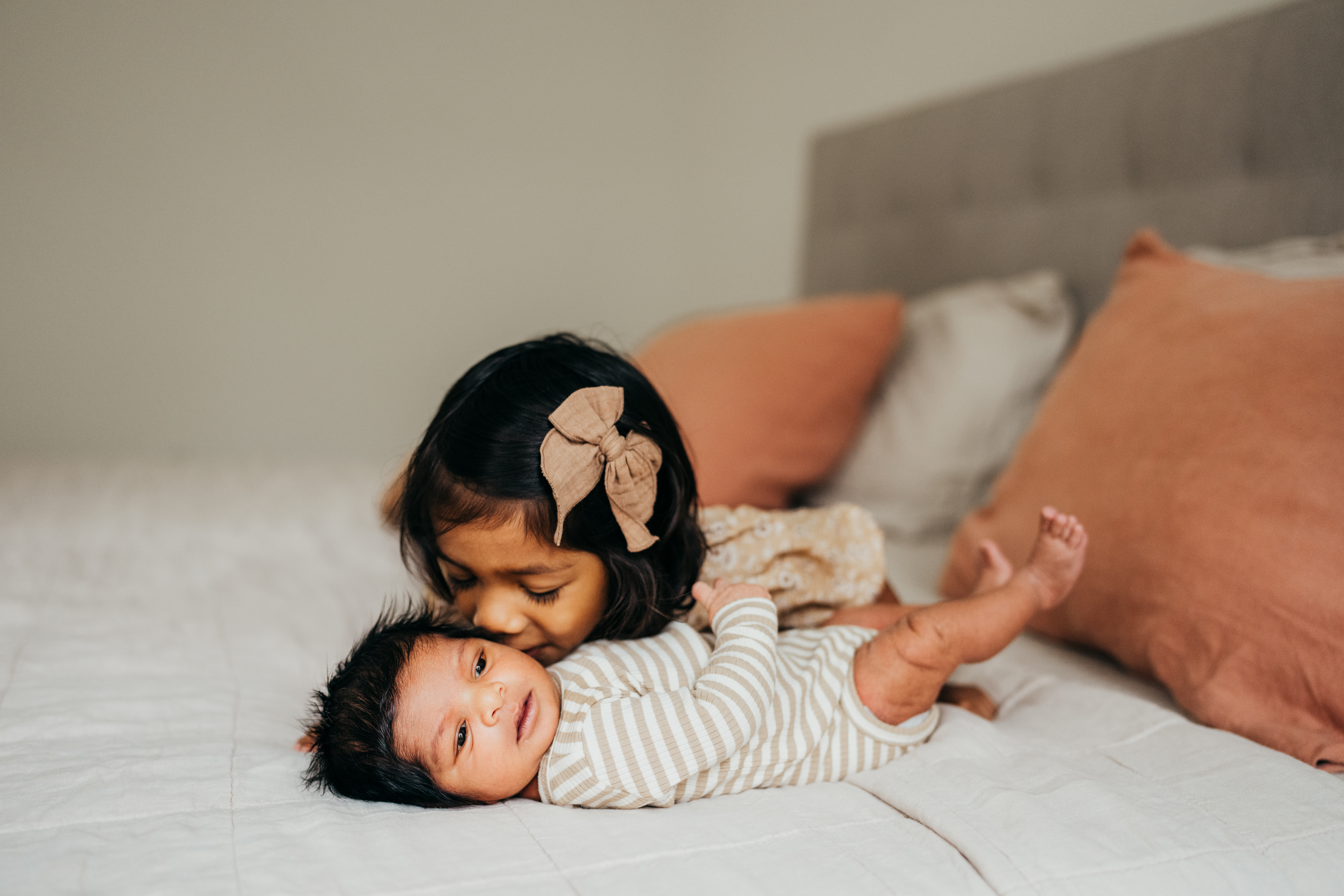 A young girl kisses her newborn baby sibling on a bed before visiting mercer island chiropractic