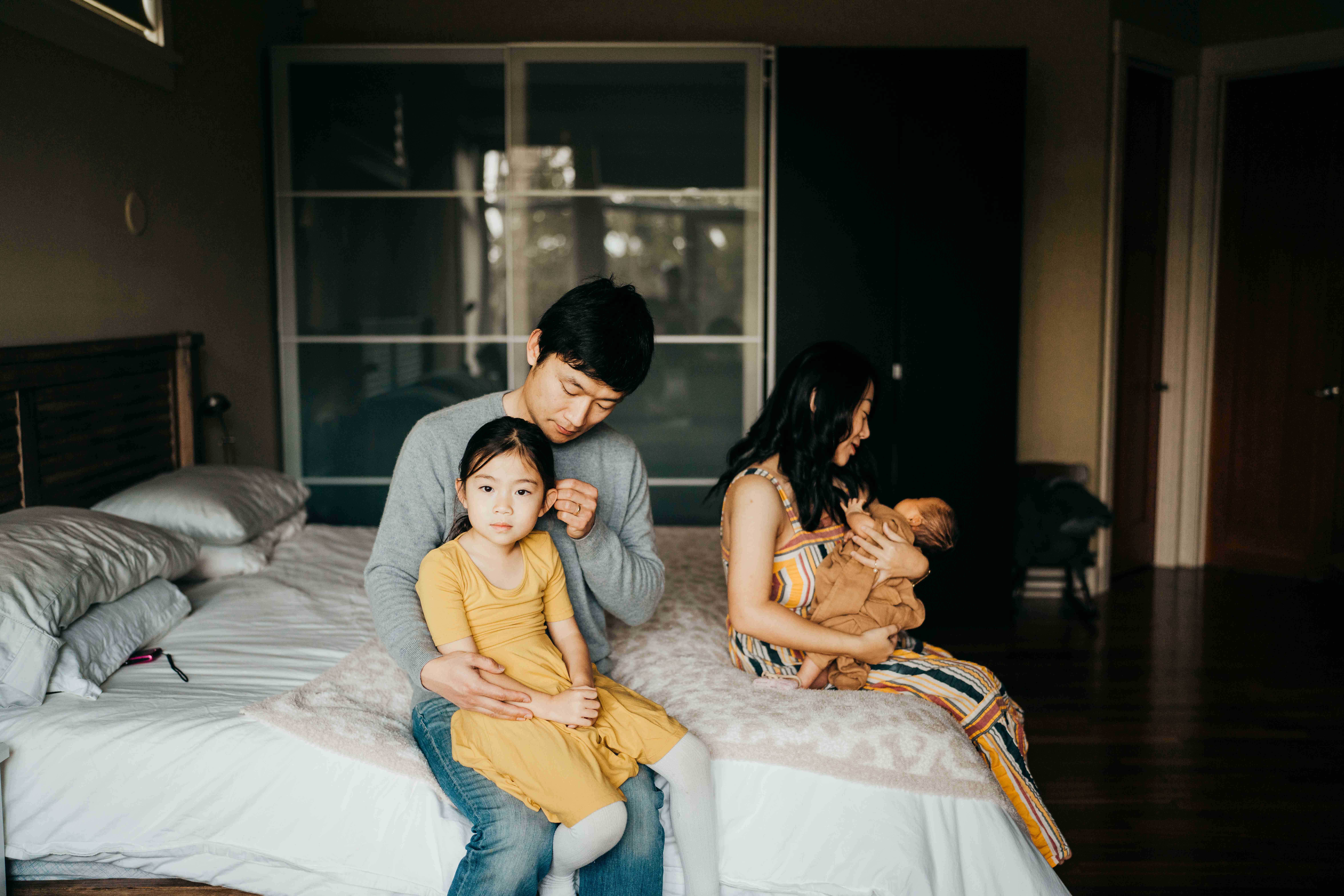 A mom and dad sit on a bed holding their toddler daughter and newborn before visiting mercer island playgrounds