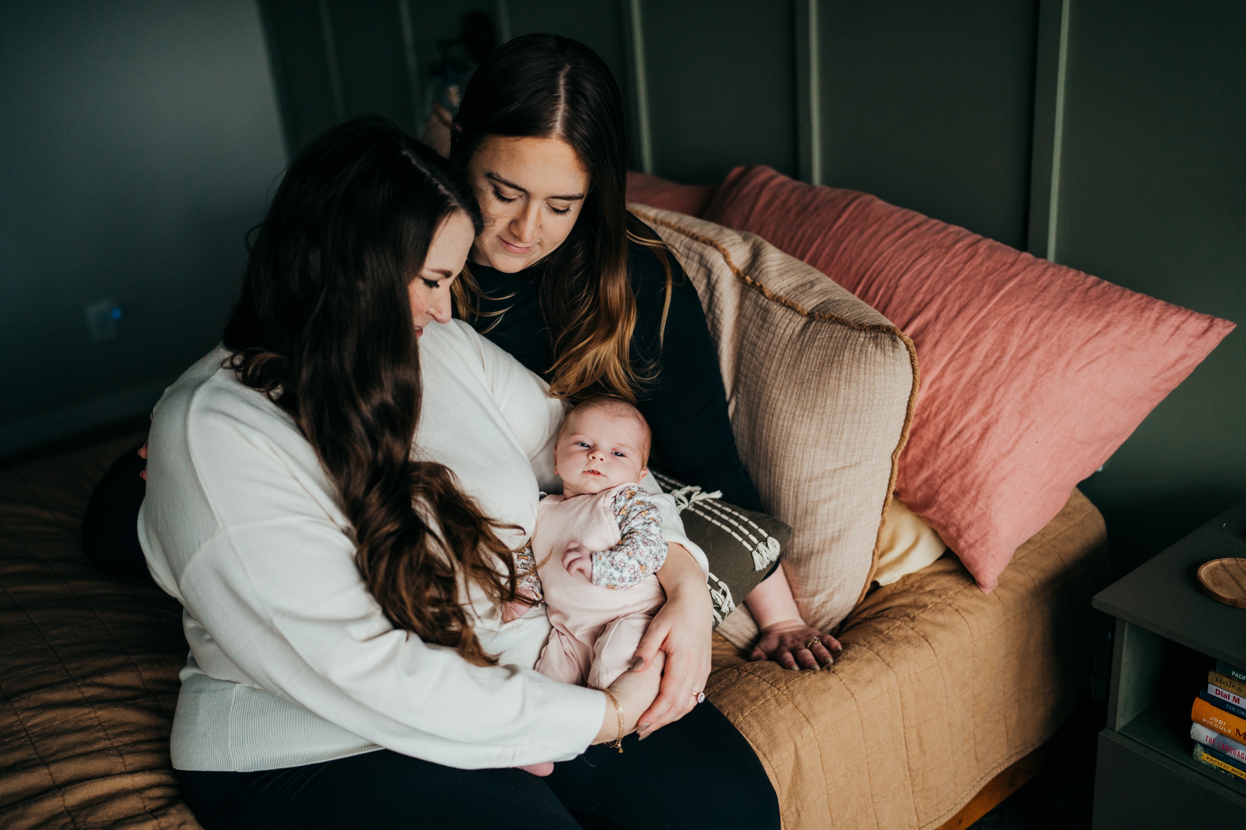 An infant lays in mom's arms in a pink onesie while sitting on a bed