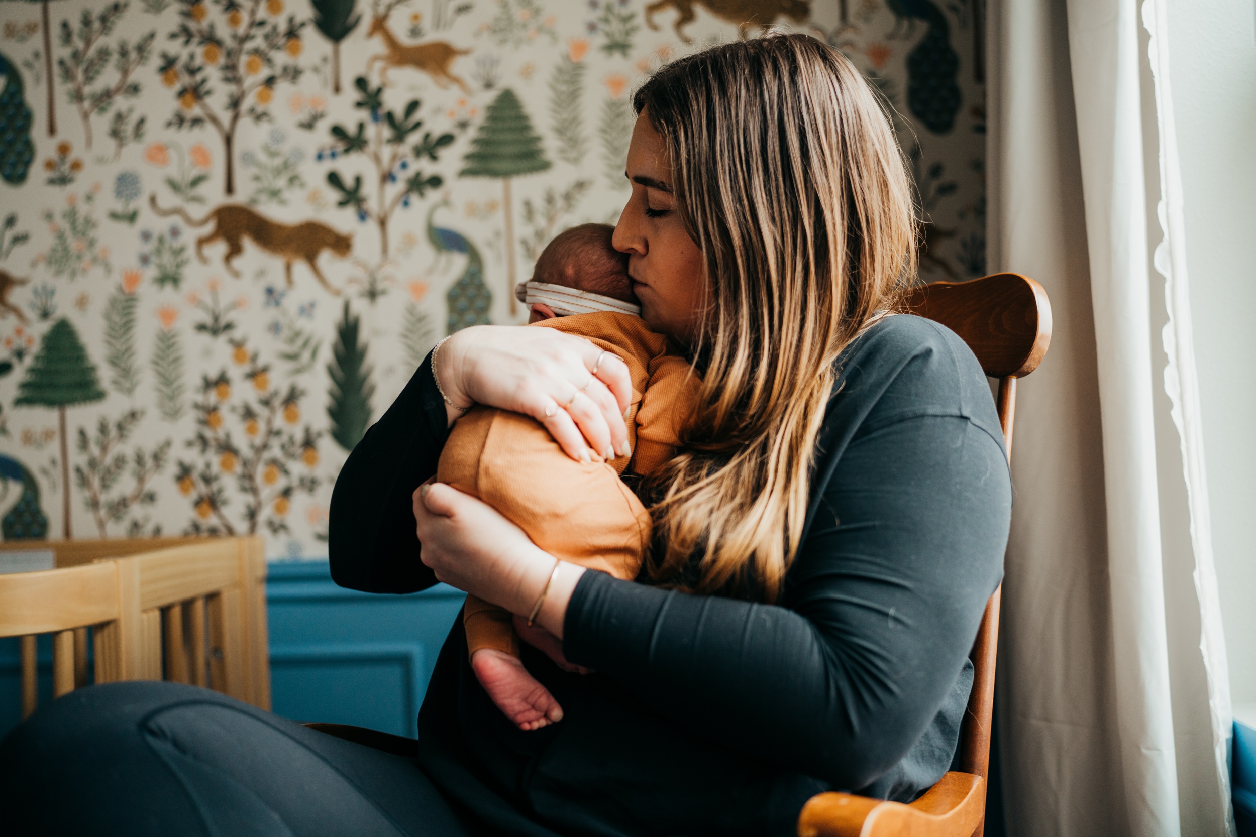 A new mom sits in a wooden rocking chair snuggling her newborn on her shoulder before some mommy and me classes in seattle
