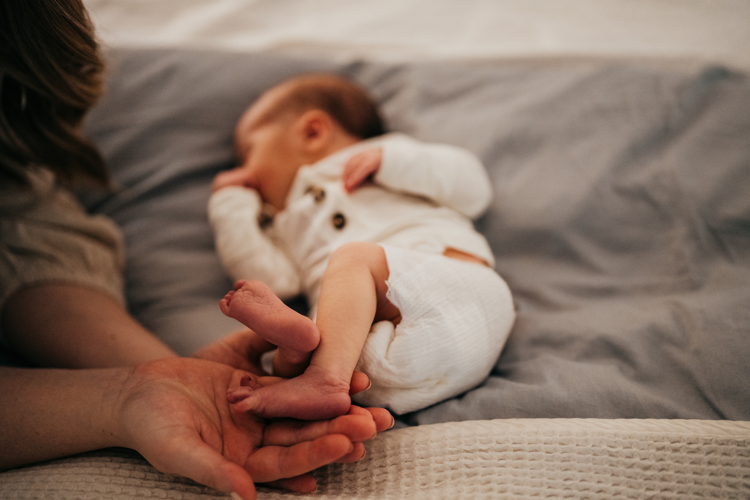 Details of mom holding her newborn's feet as it sleeps on a bed after visiting pediatric chiropractors in seattle