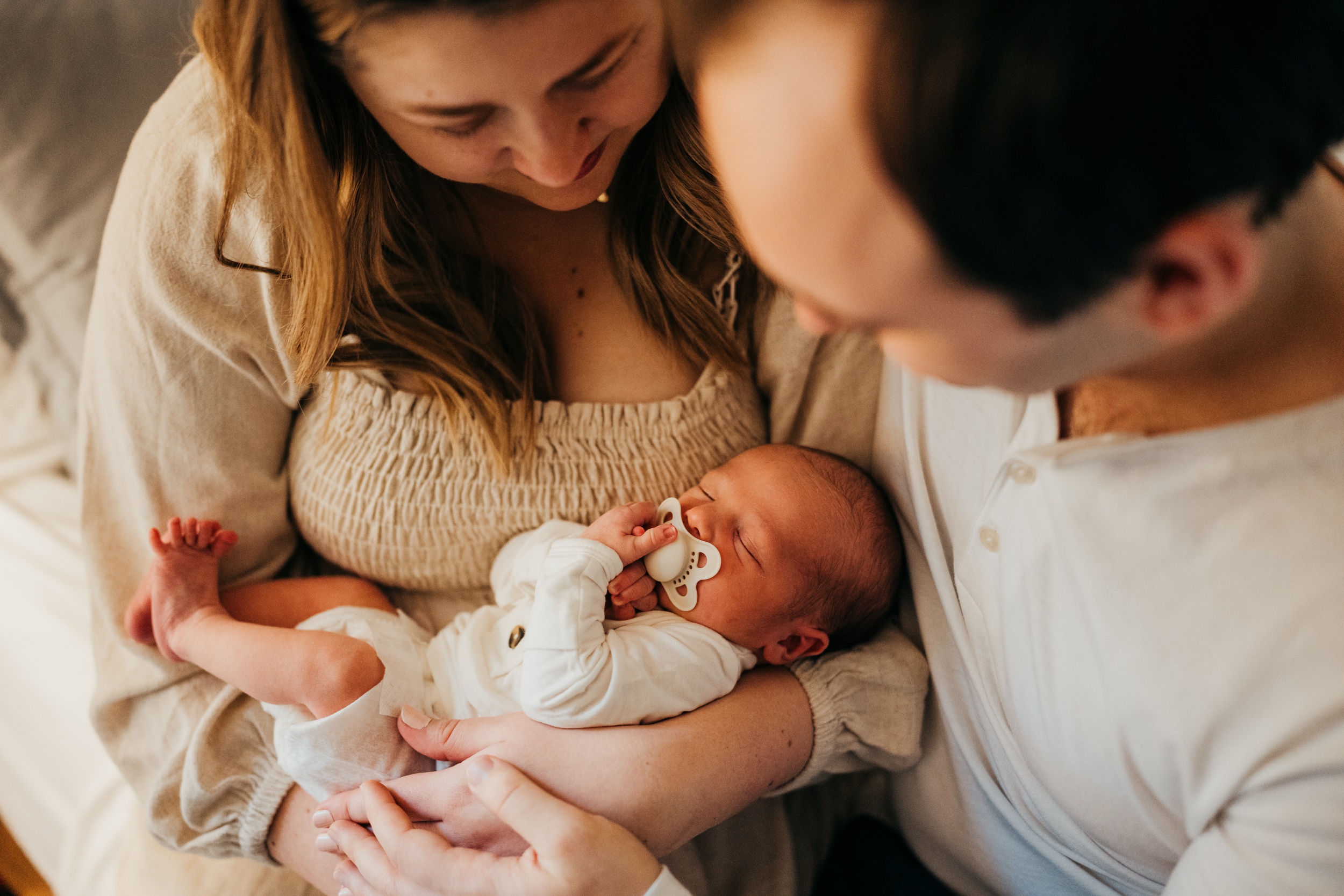 Happy new parents snuggle over their sleeping newborn in mom's arms on a bed after finding placenta encapsulation in seattle