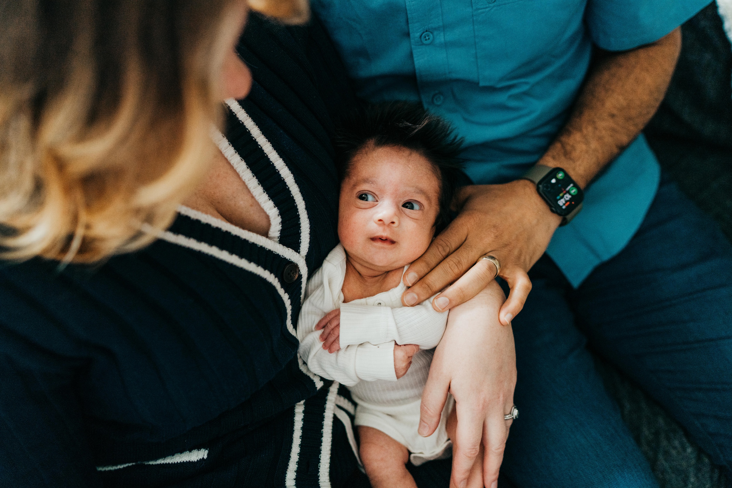 A. newborn baby lays in mom and dad's lap while looking up at mom after some prenatal yoga in seattle