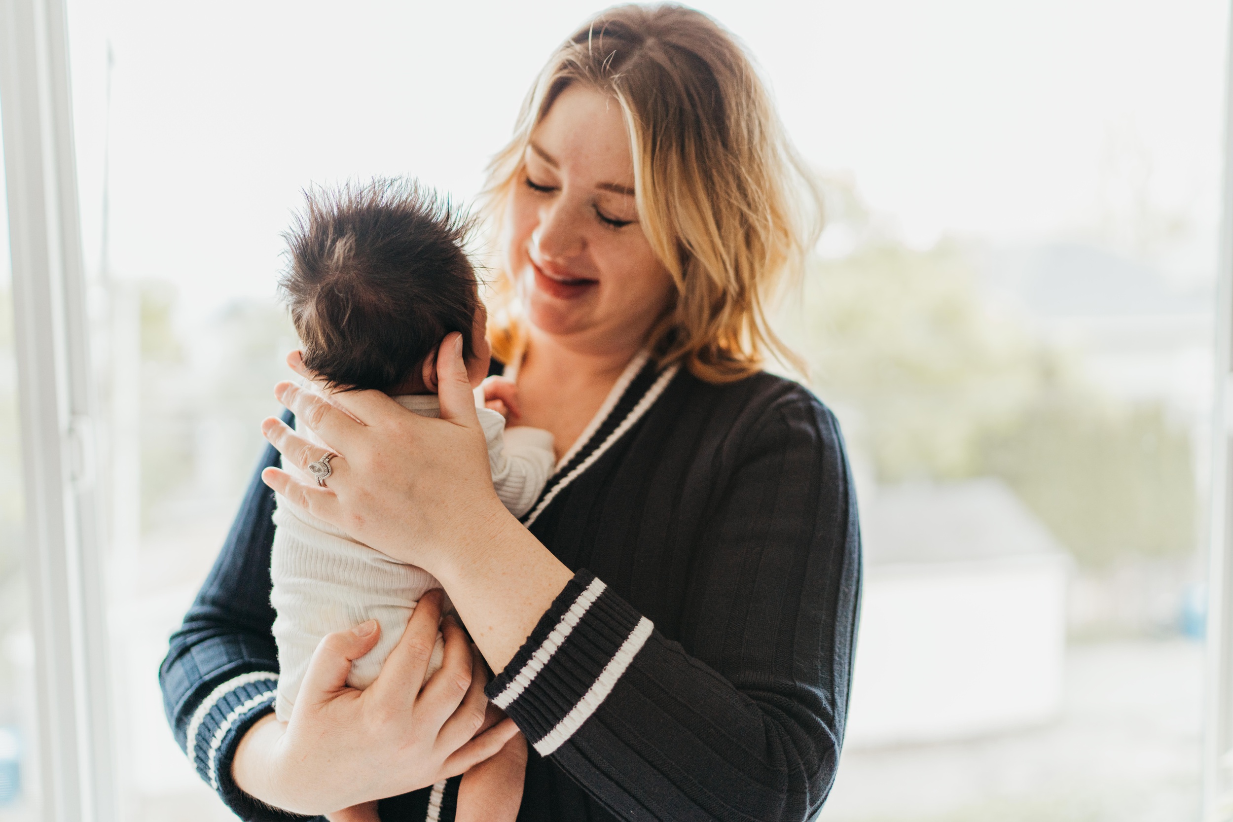 A happy mom snuggles her newborn baby while standing in a window after some prenatal yoga in seattle