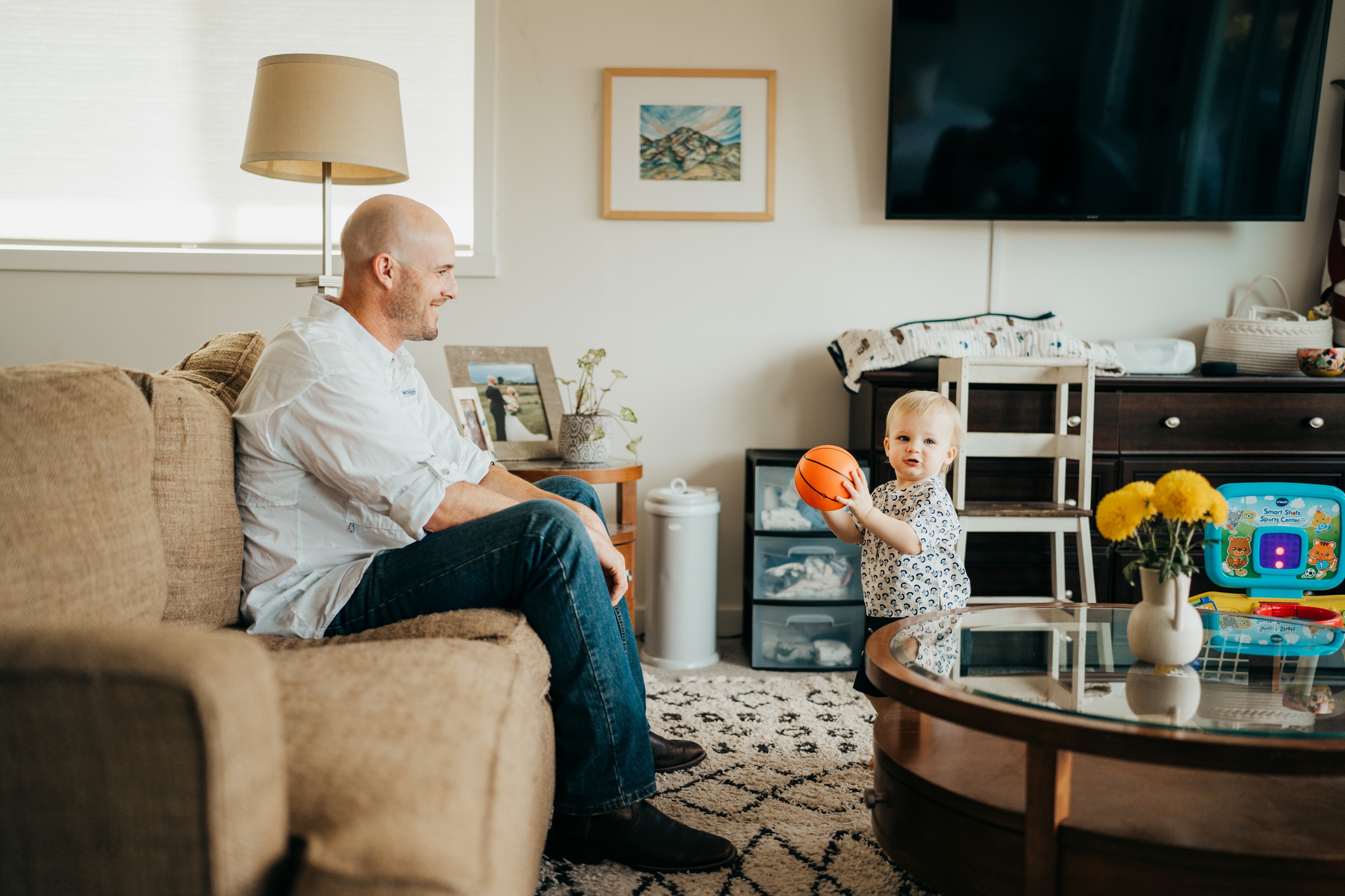 An infant plays basketball with dad in the living room