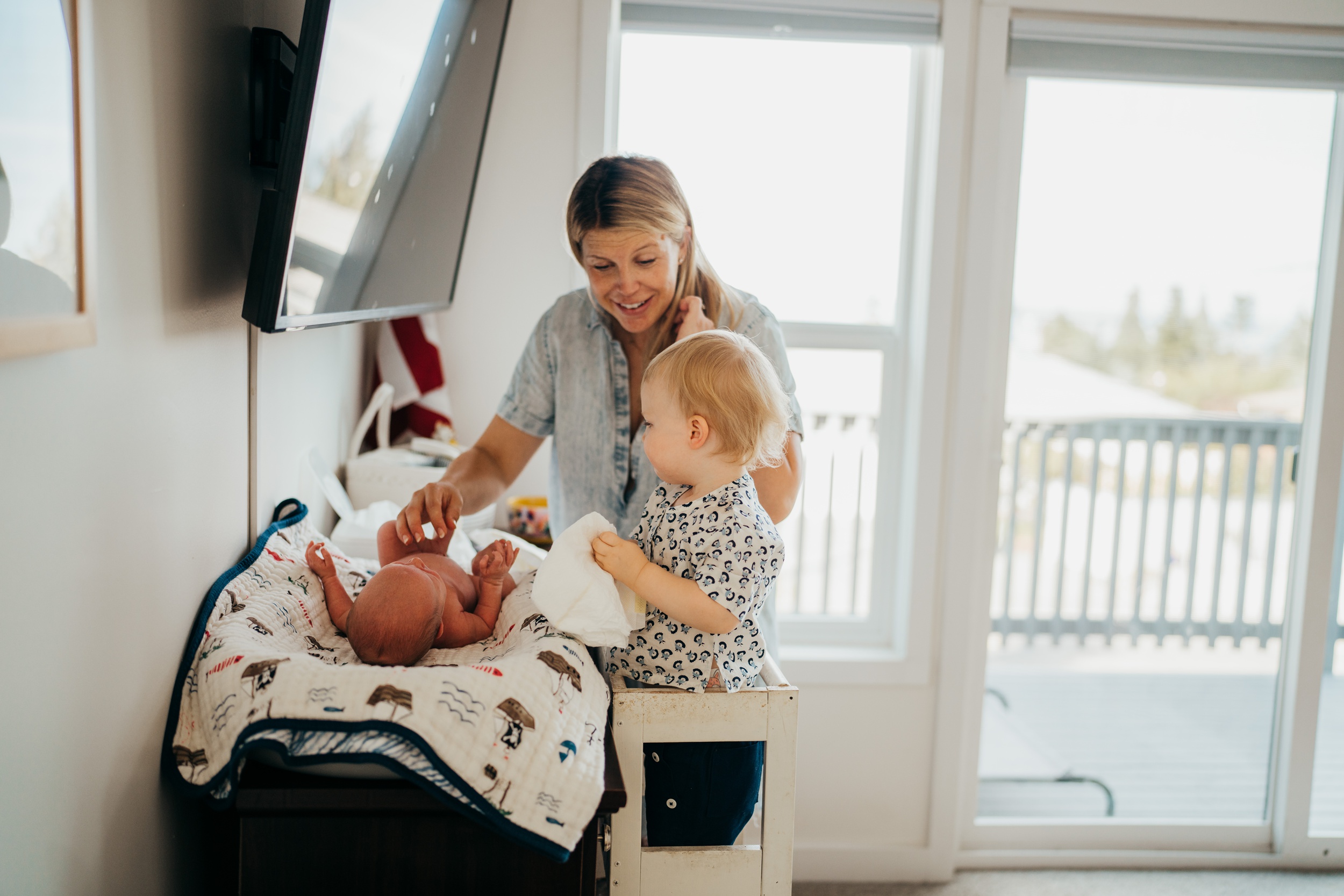 A happy mom helps her infant on a high chair change the newborn's diaper before some swim lessons on mercer island