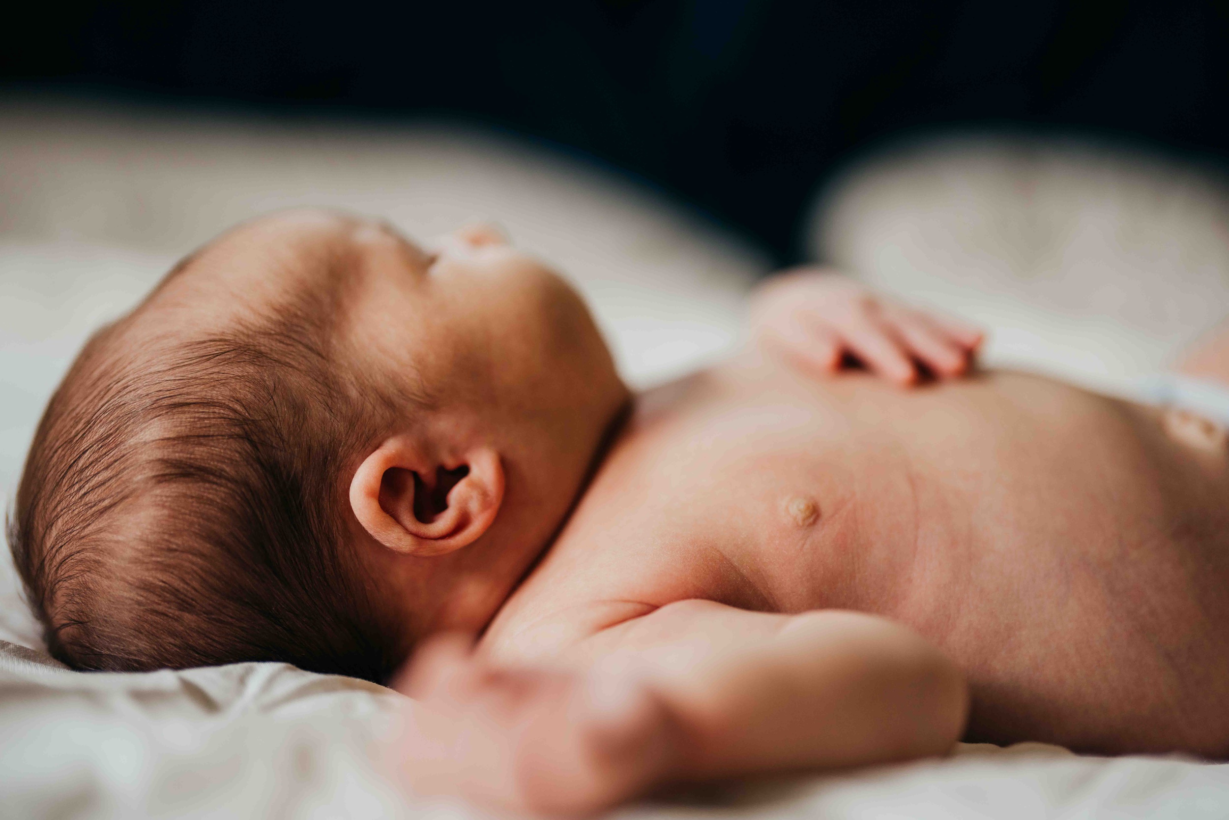 Details of a newborn baby laying shirtless on a bed before some baby yoga in seattle