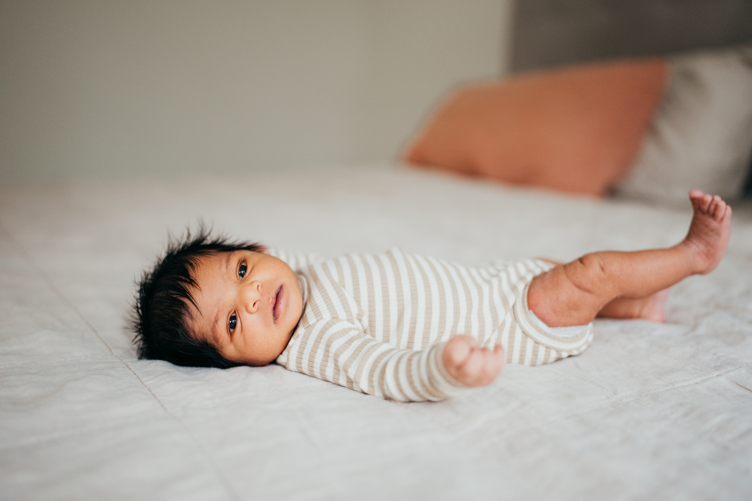 A newborn baby lays on a bed in striped onesie with eyes open before some baby yoga in seattle