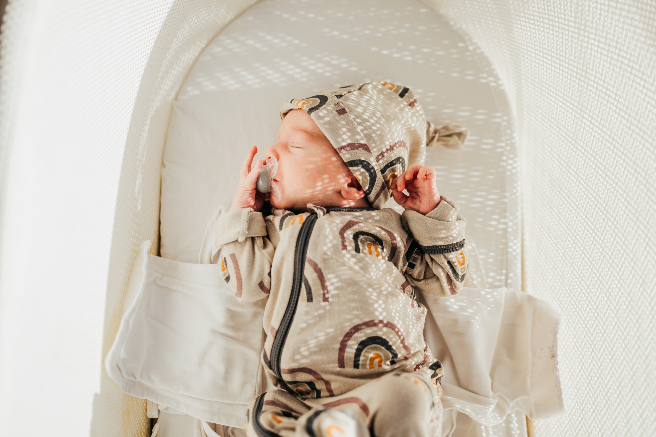 A newborn baby sleeps in a rainbow onesie in a crib after visiting bootyland kids