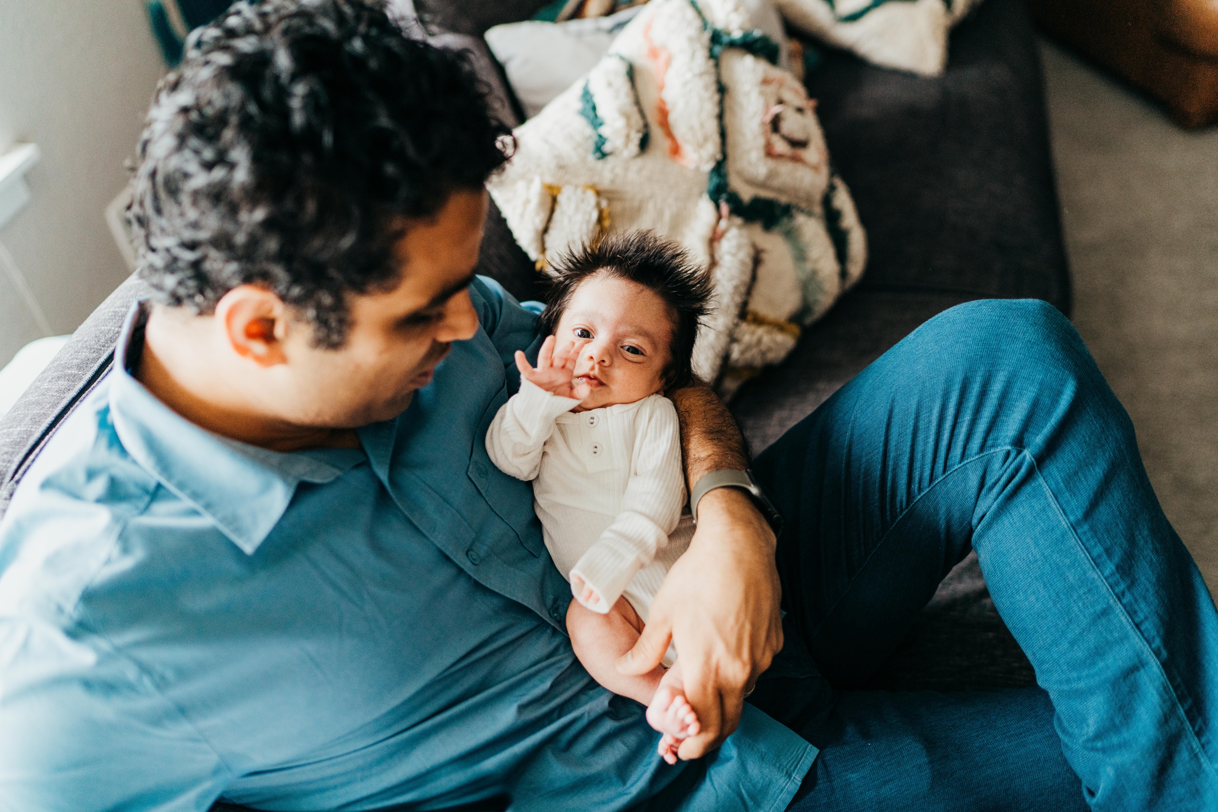 A newborn baby waves his hand while laying in dad's arms