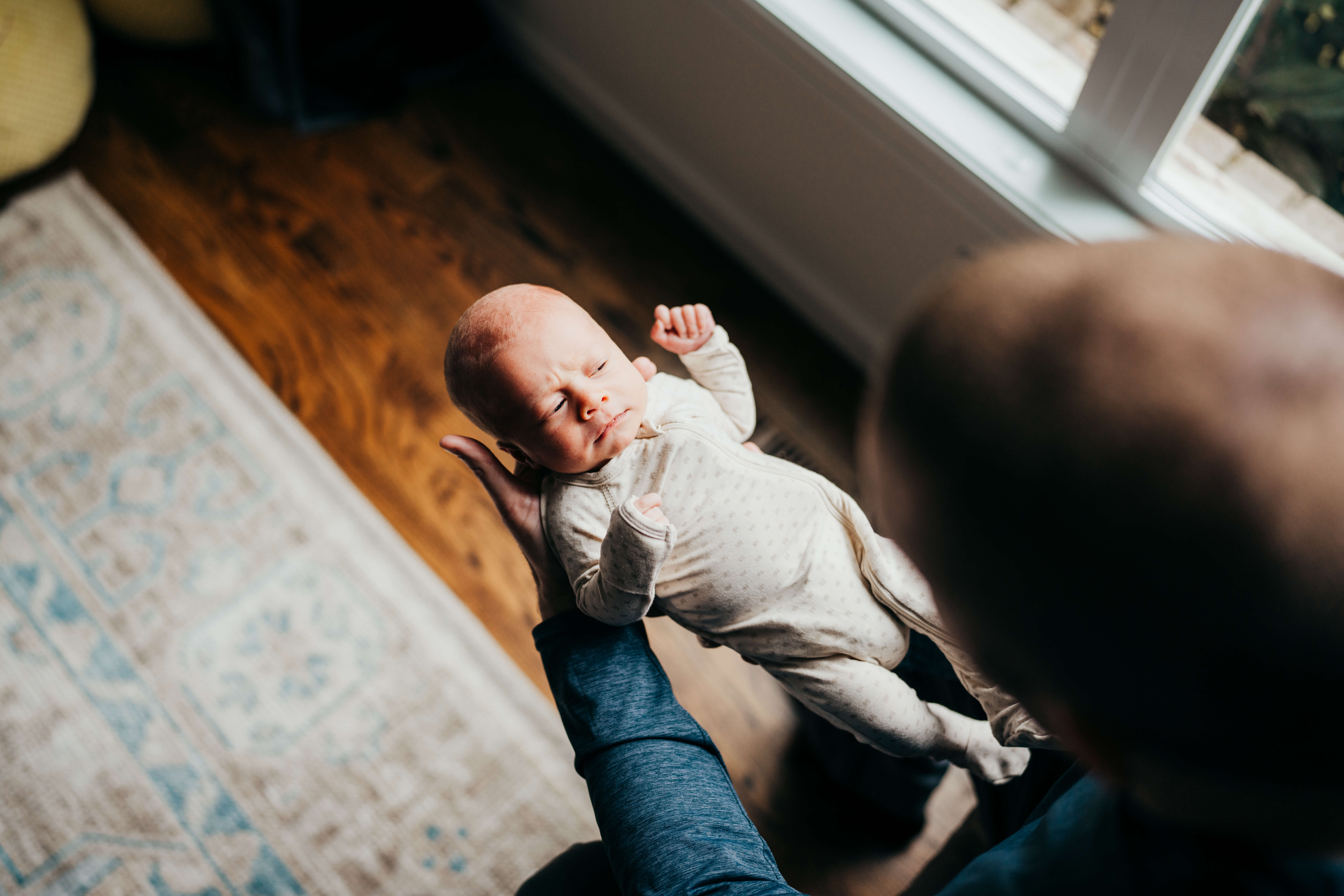 A look over the shoulder of dad as he stands in a window gazing down at his newborn baby in his hands thanks to Puget Sound Birth Center