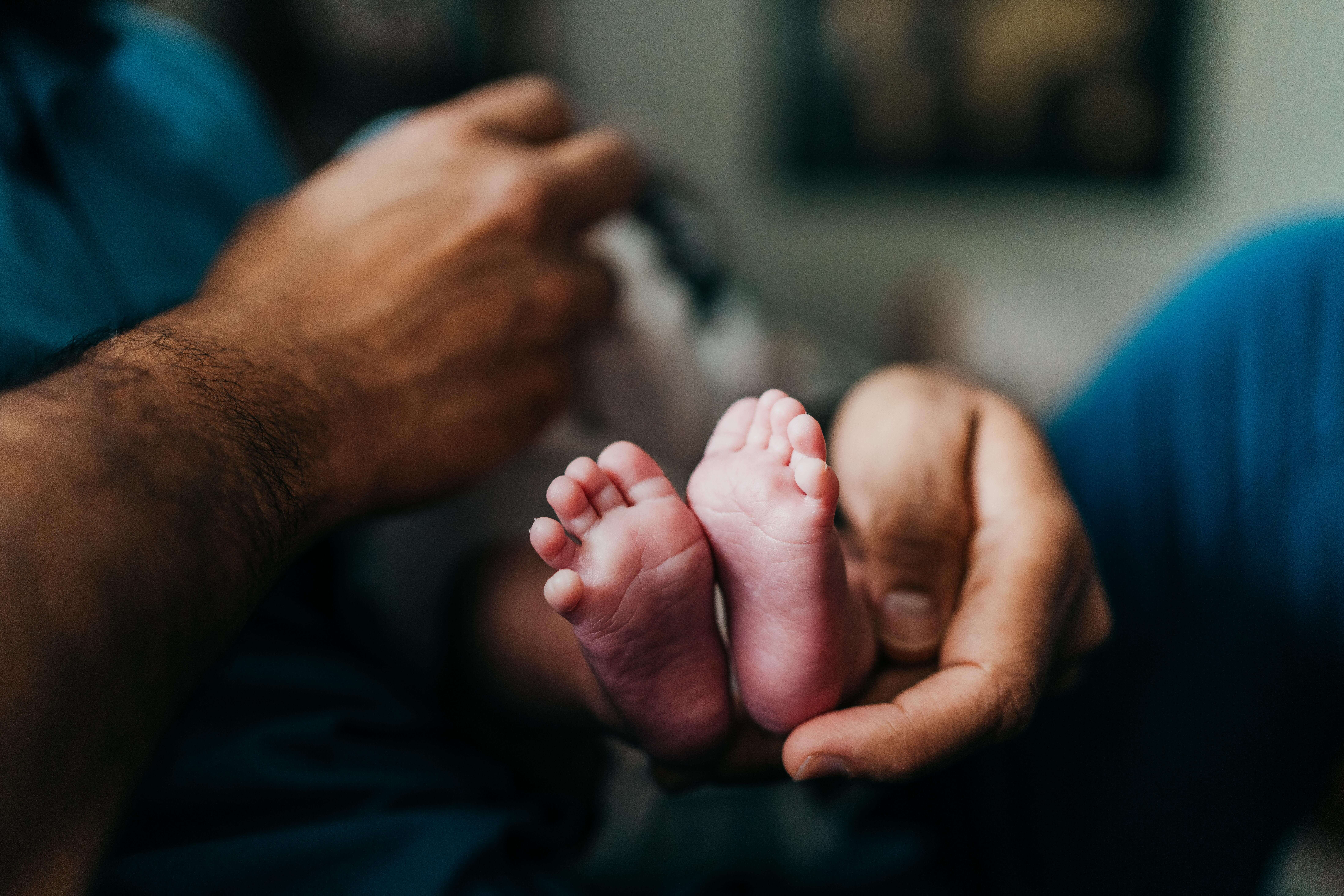 details of a newborn baby's feet in dad's hand and lap