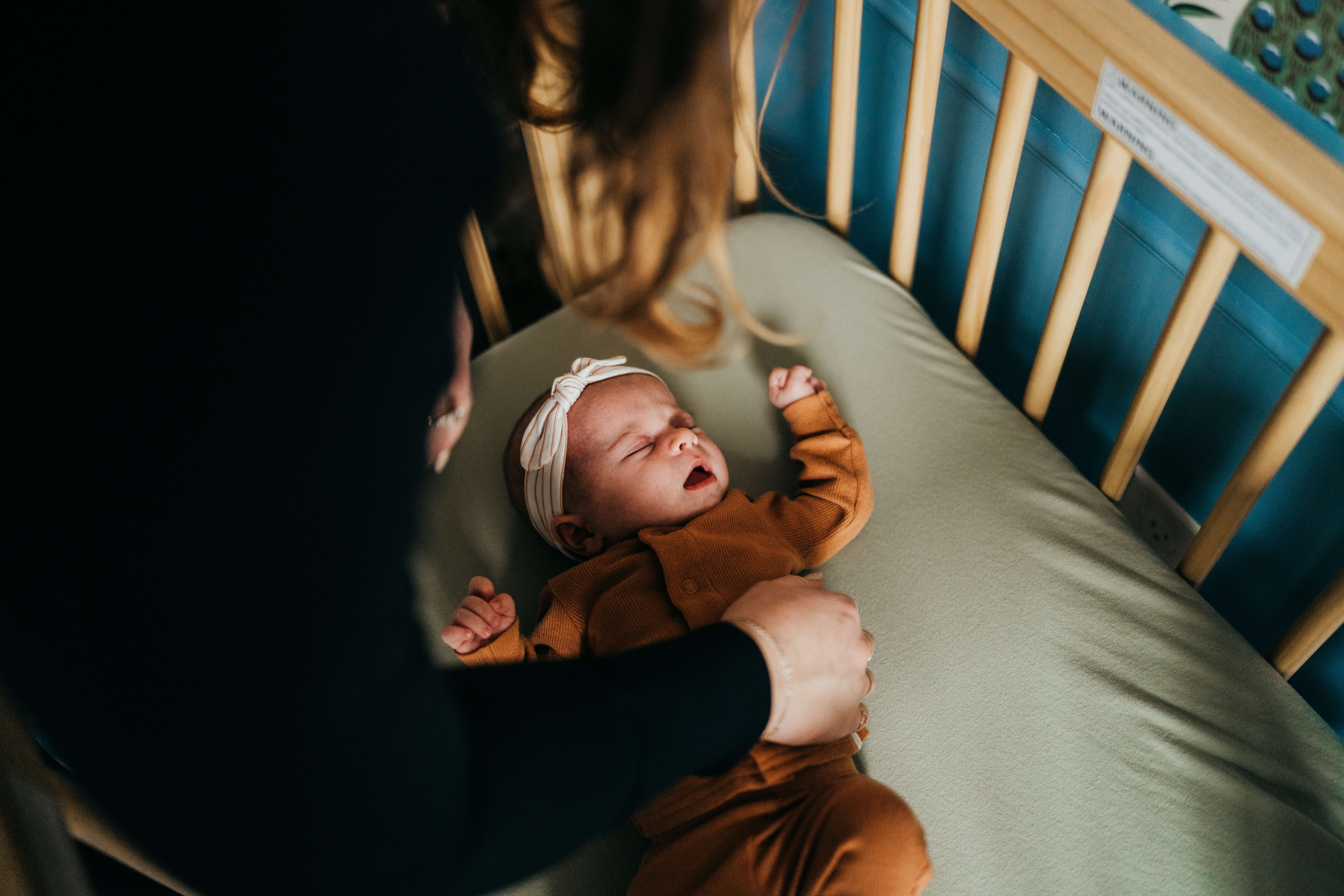 Mom puts her newborn baby girl in an orange onesie to bed in the crib