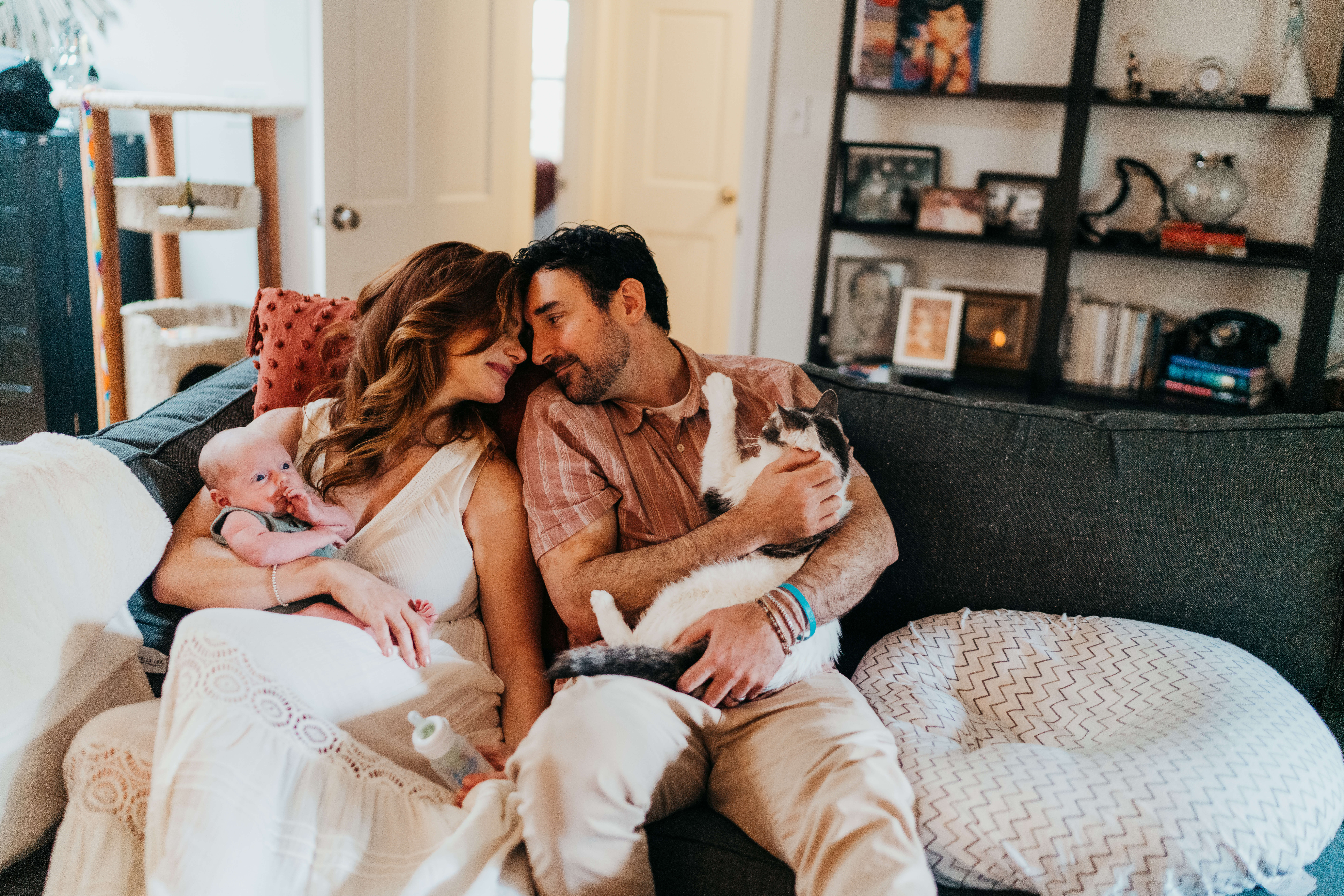 happy new parents snuggle on a couch while mom holds their newborn and dad their cat