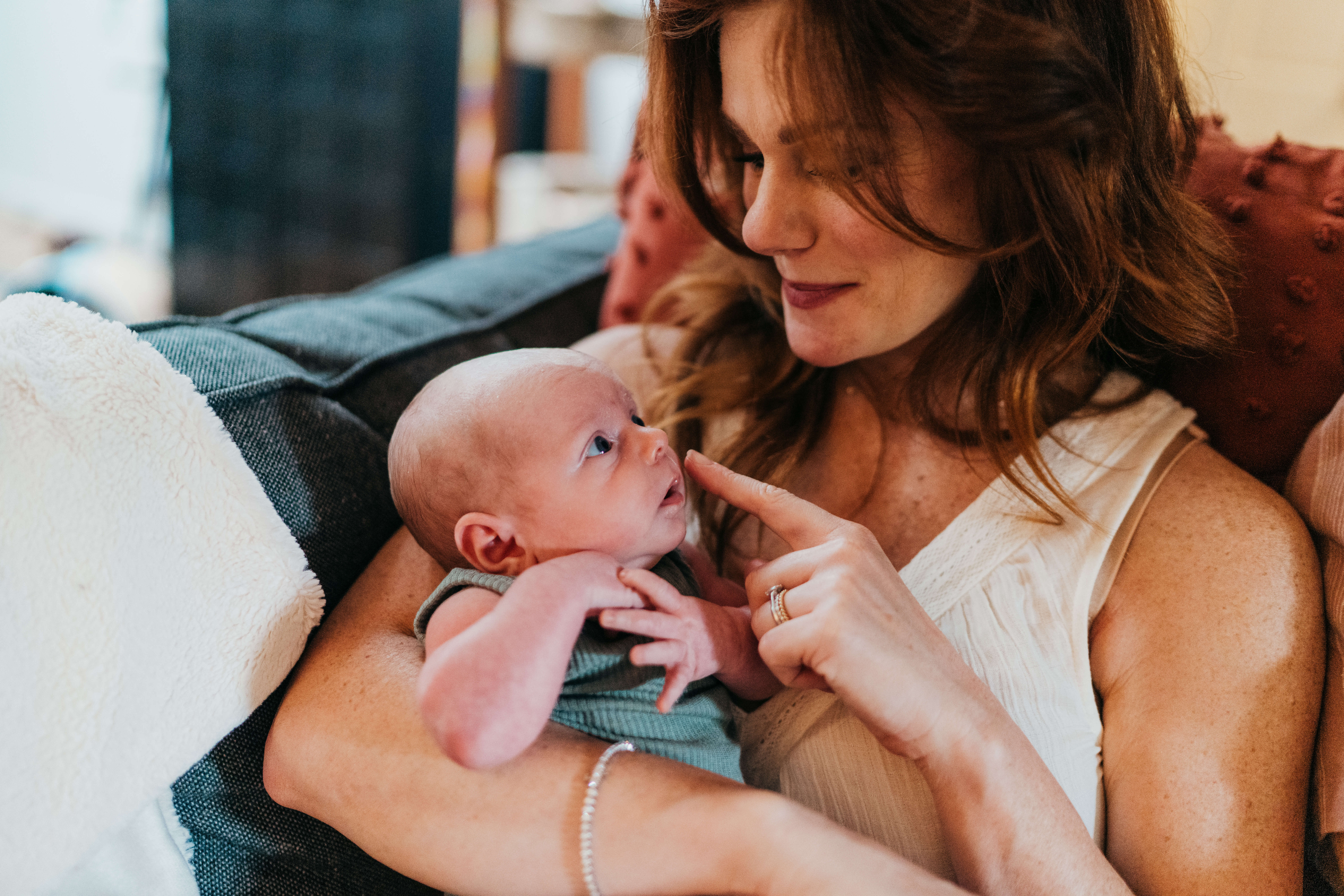 A newborn baby looks up to mom as she boops the baby nose while snuggling on a couch after meeting lactation consultants on mercer island
