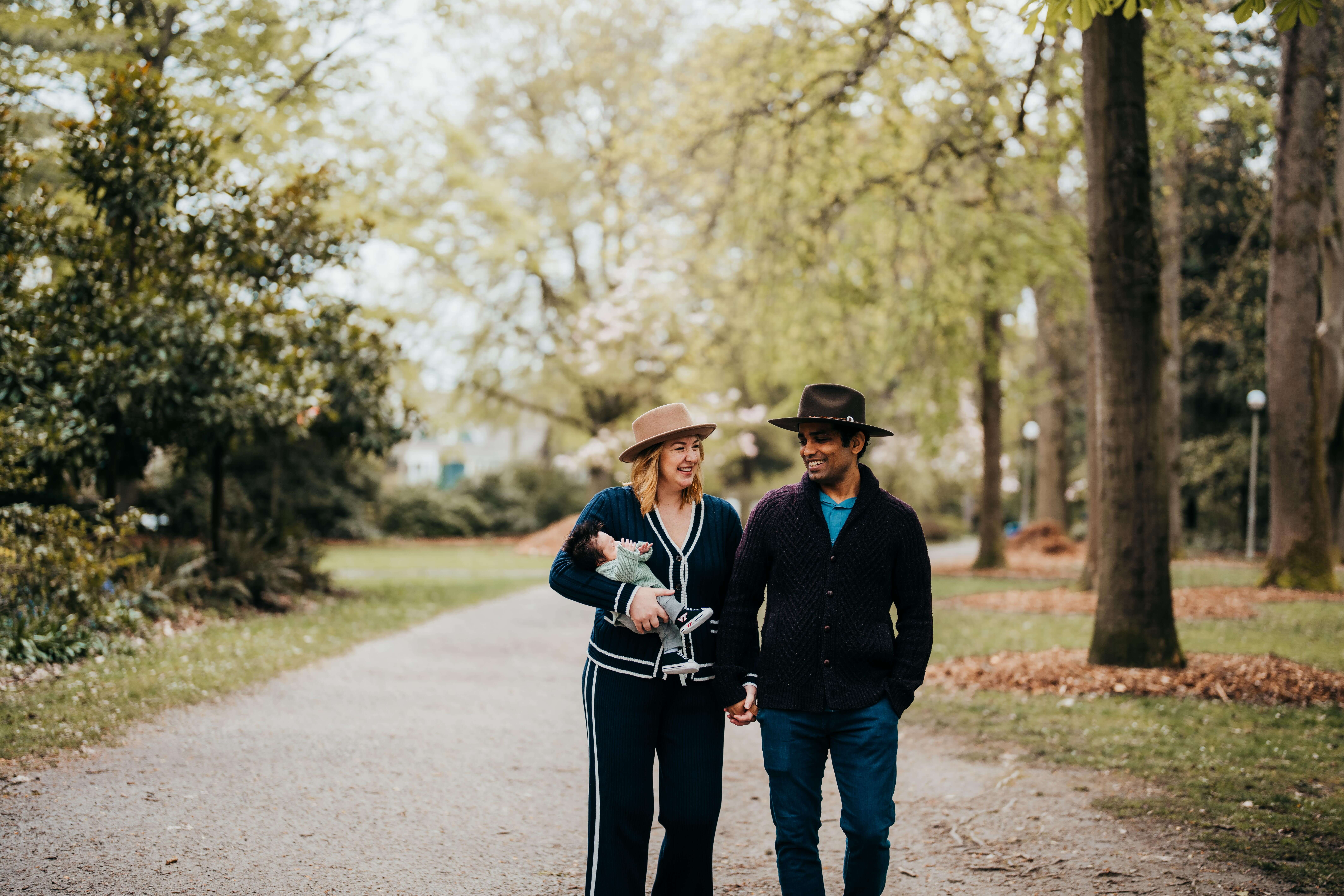Happy new parents walk in a park carrying their newborn and laughing together holding hands after visiting Chrysanthemum seattle