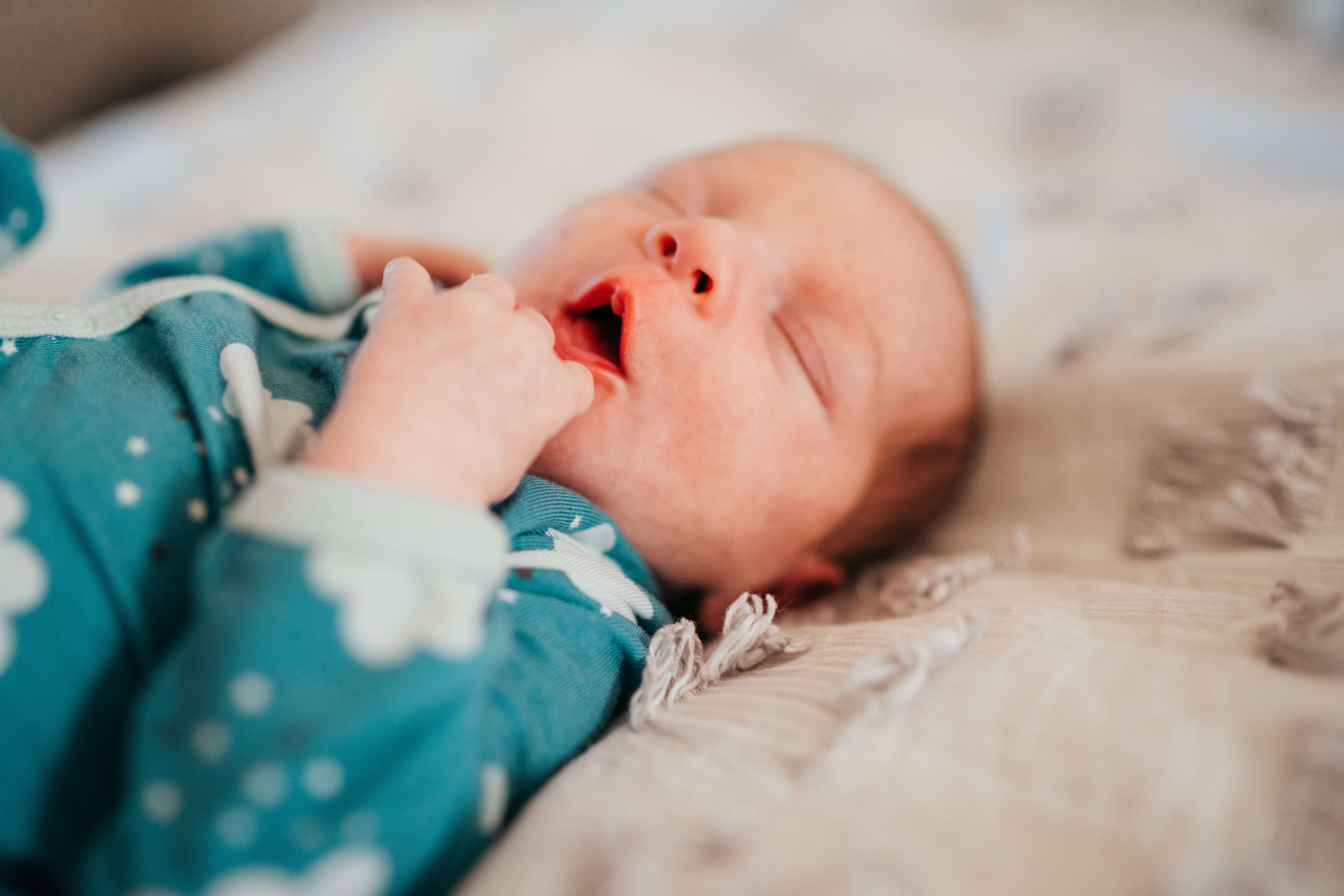 A sleeping newborn in a blue onesie on a bed with mouth open after visiting The Original Children's Shop