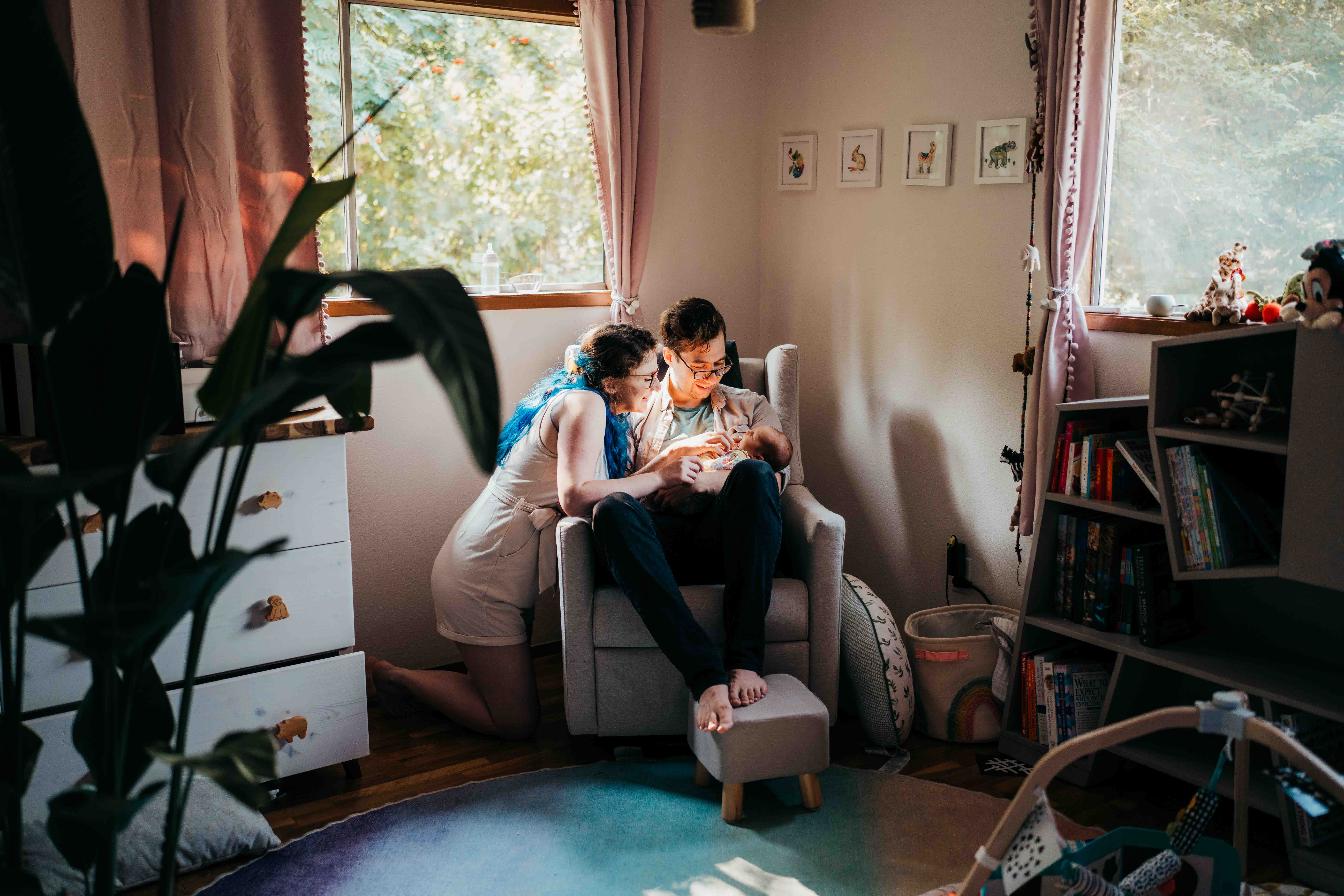 New mom and dad snuggle in a nursing chair with their newborn in dad's lap after using