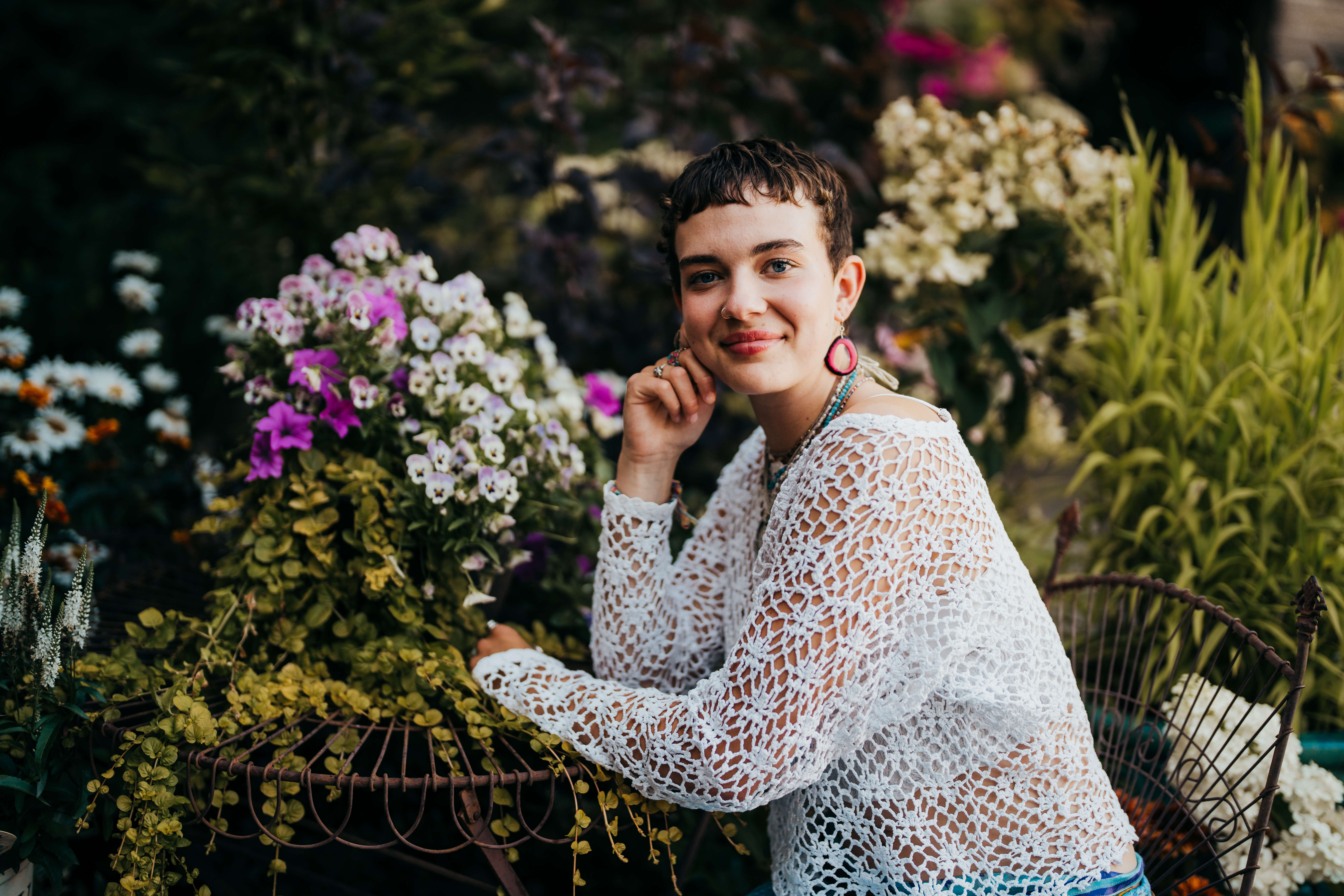 A woman in a lace sweater leans on a garden table while smiling