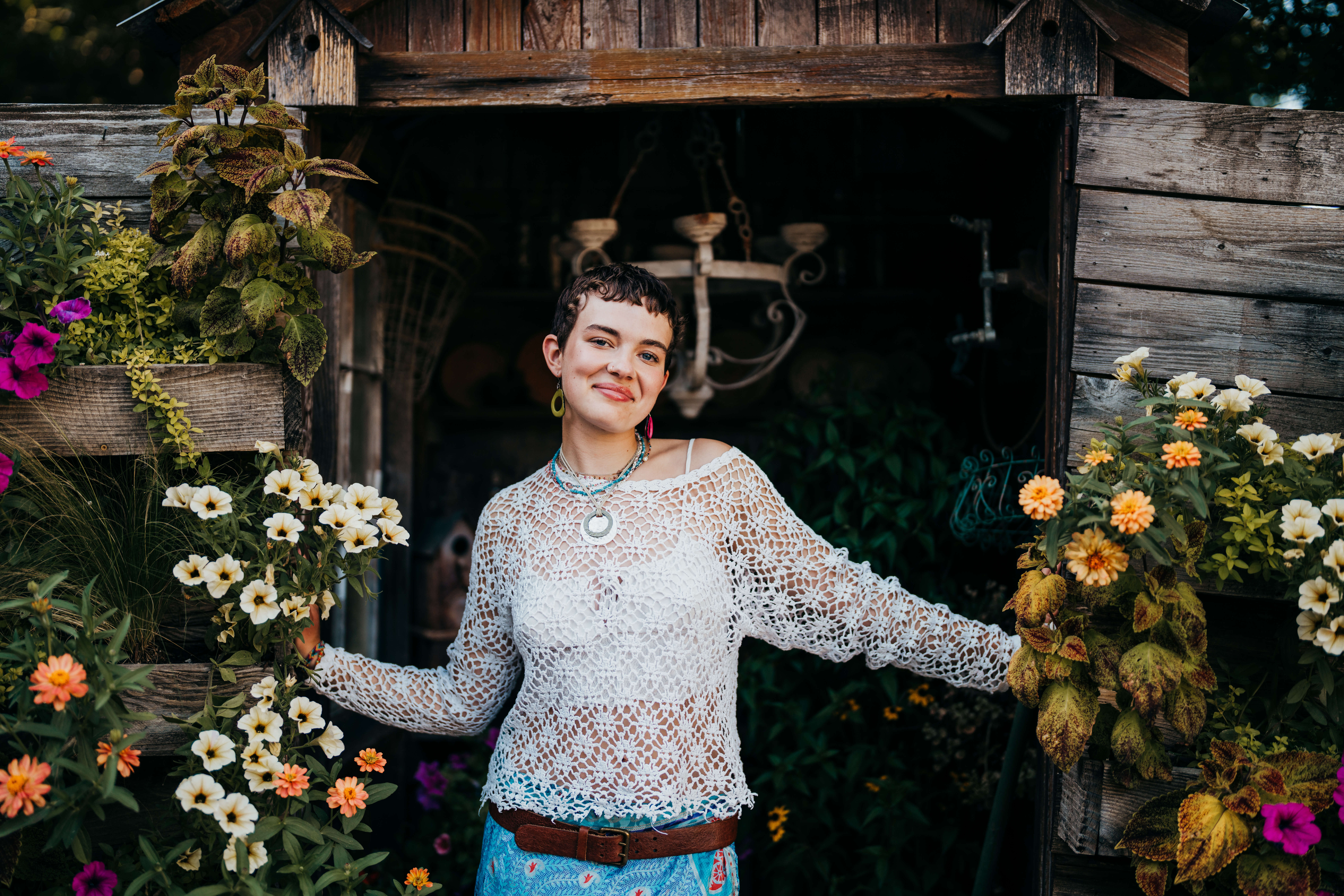 a high school senior in a lace blouse and bright skirt stands in a garden shed entrance smiling after visiting college fairs in seattle