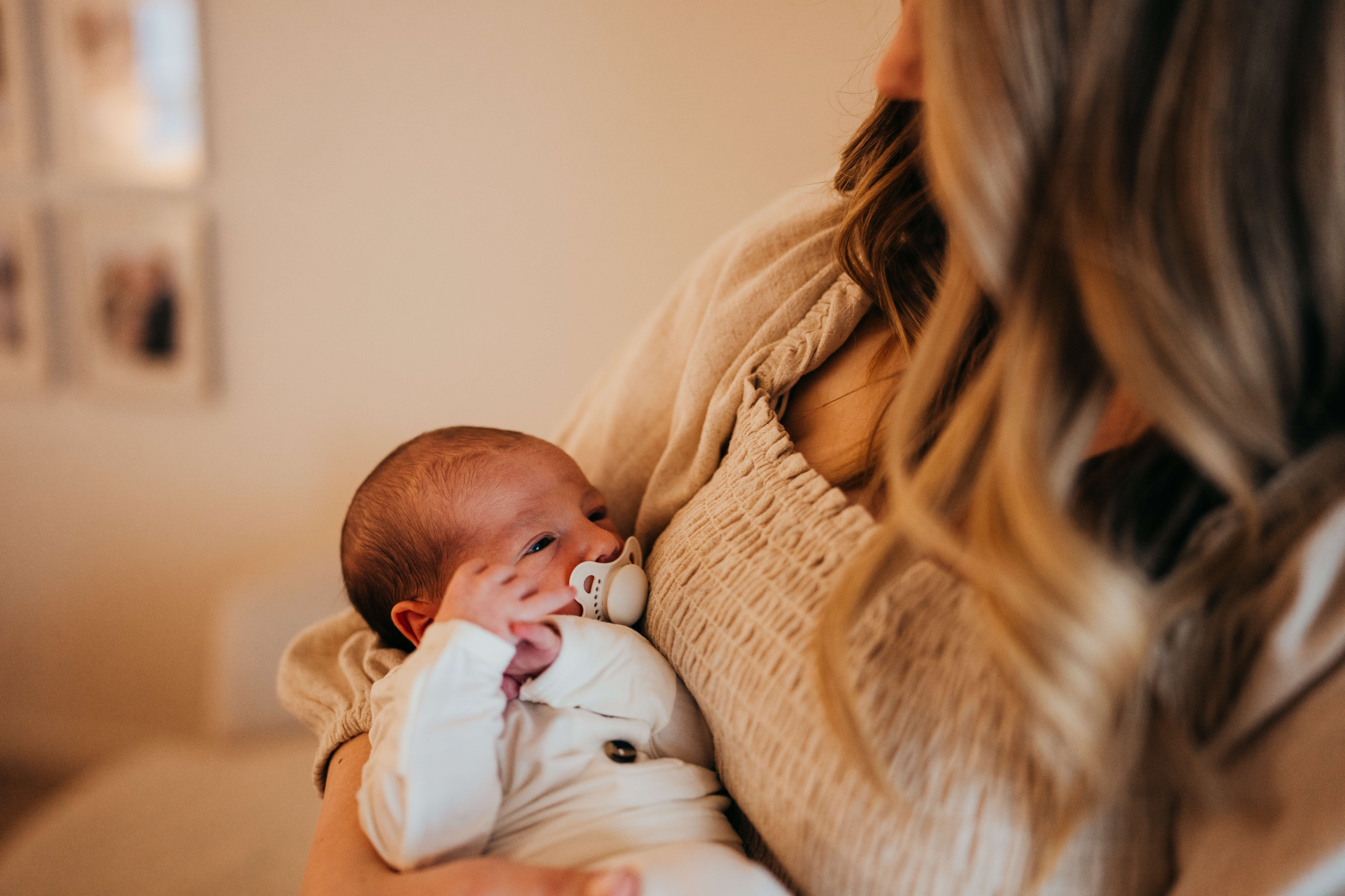 a newborn baby lays in mom's arms against her chest in a white onesie