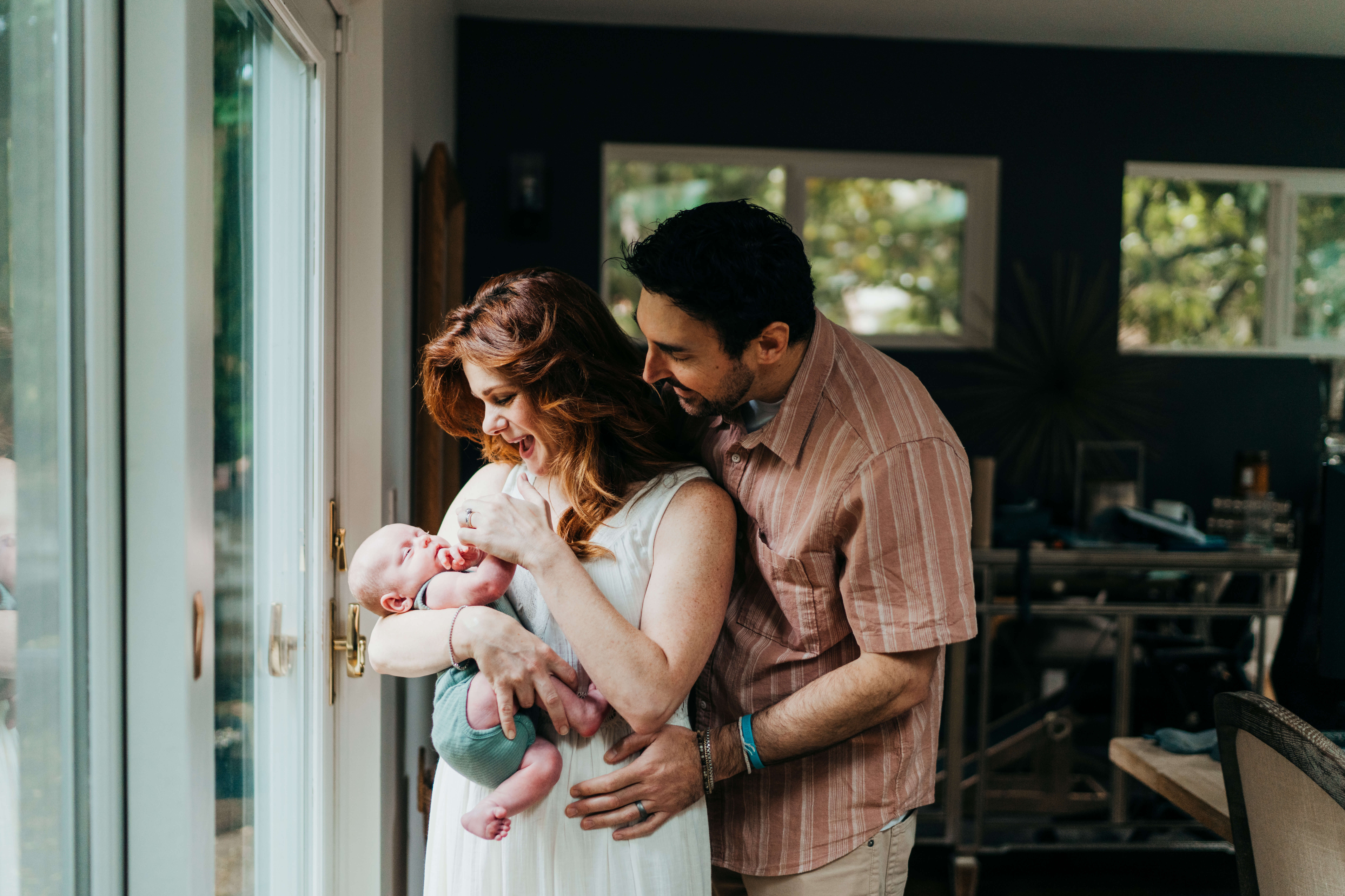 A mom and dad stand in their back glass door playing with their newborn in mom's arms thanks to ivf in seattle