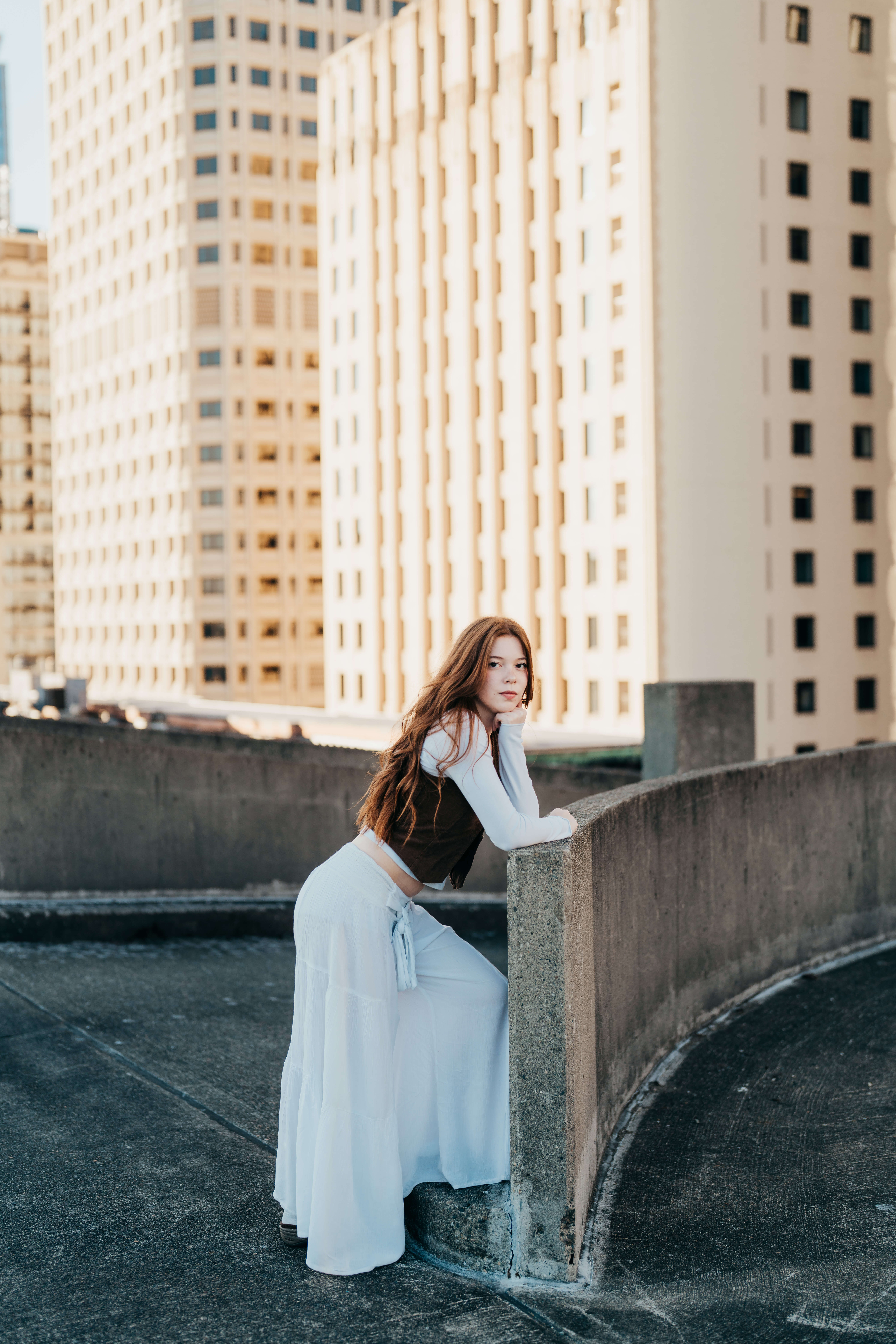A high school senior leans on a parking garage railing in a white skirt after visiting Colleges In Downtown Seattle