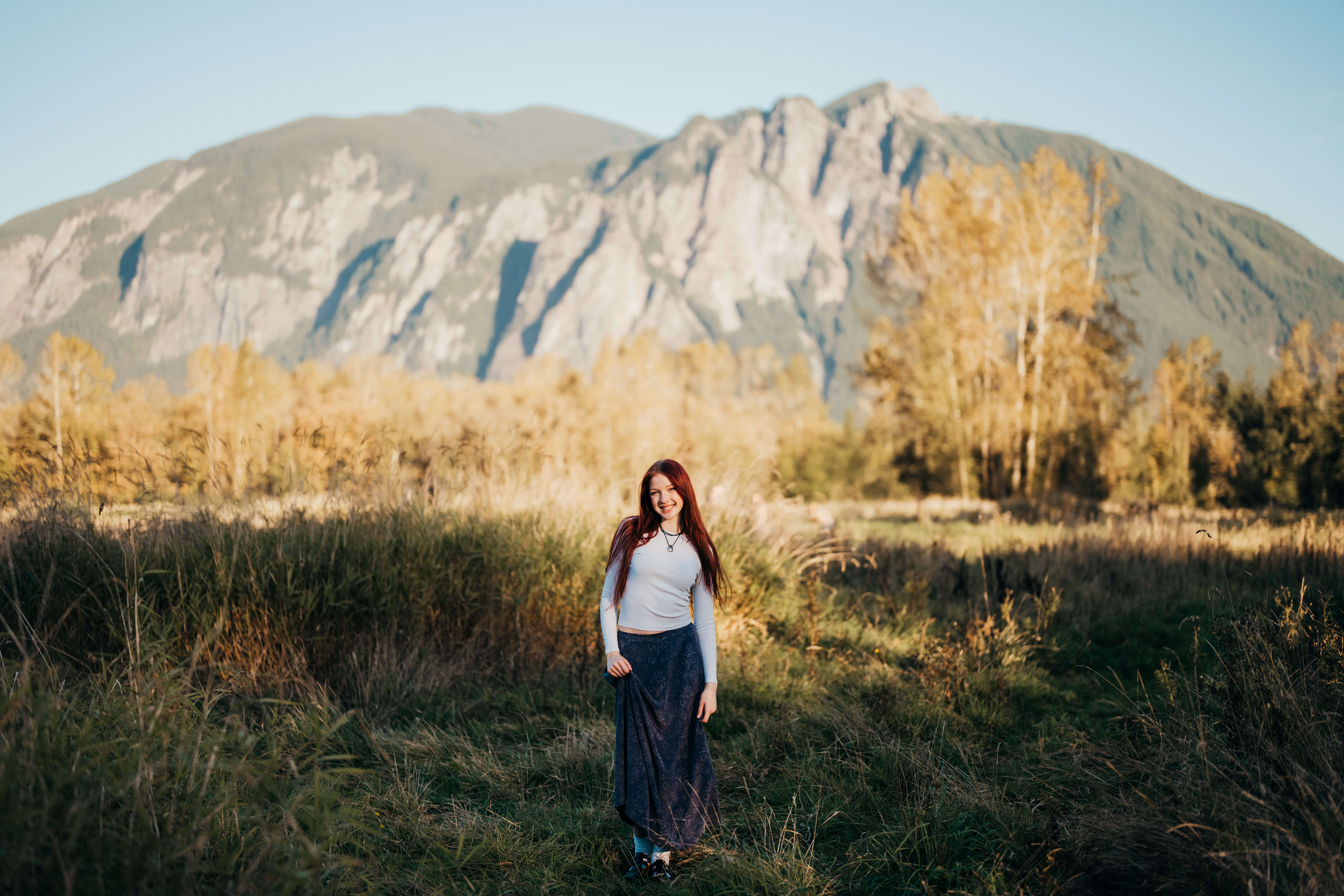 A high school senior in a white shirt walks in a meadow of tall grasses after exploring Colleges In Downtown Seattle