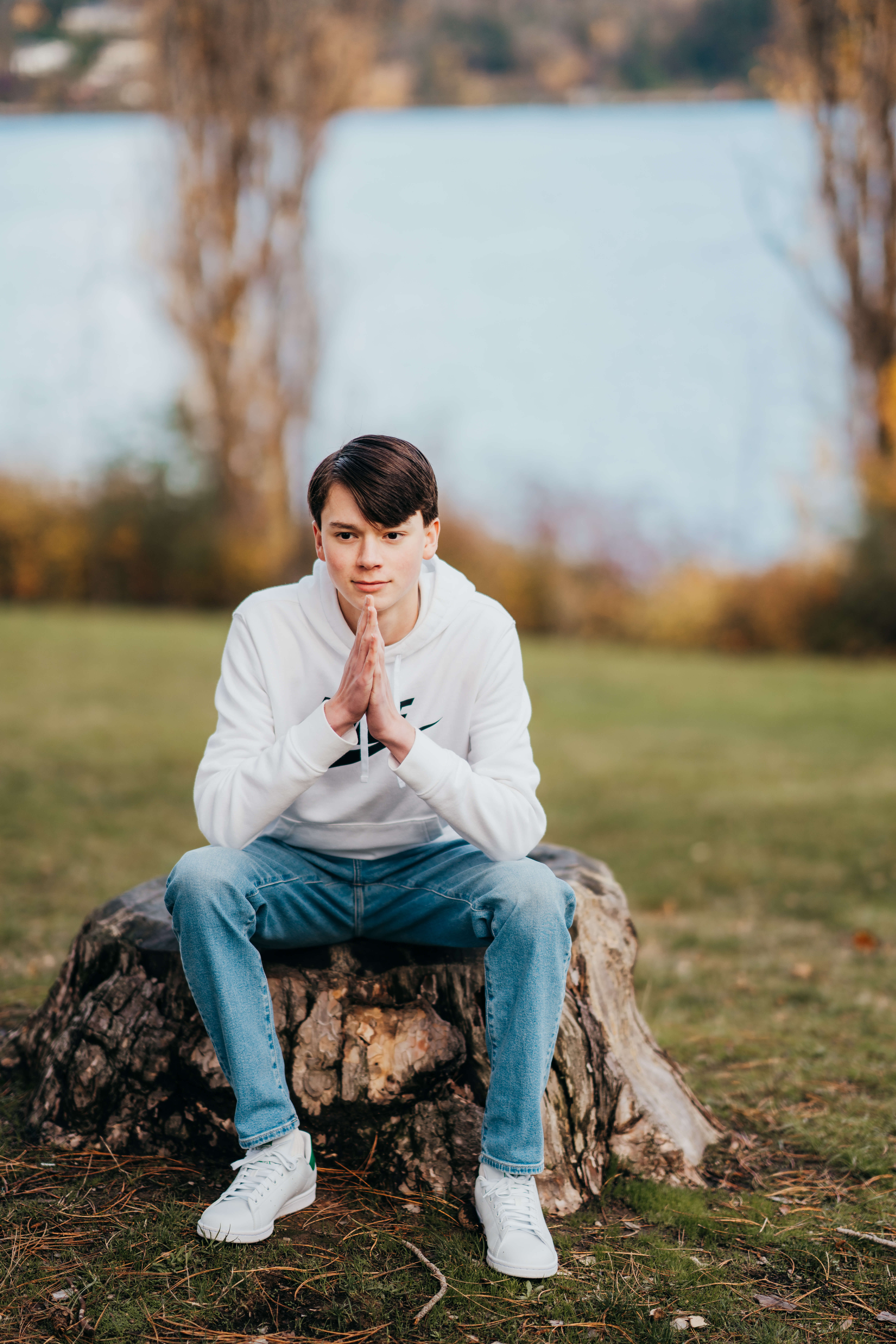 A teenage boy in a white hoodie and jeans sits on a tree stump leaning on his elbows after applying to High School Internships In Seattle