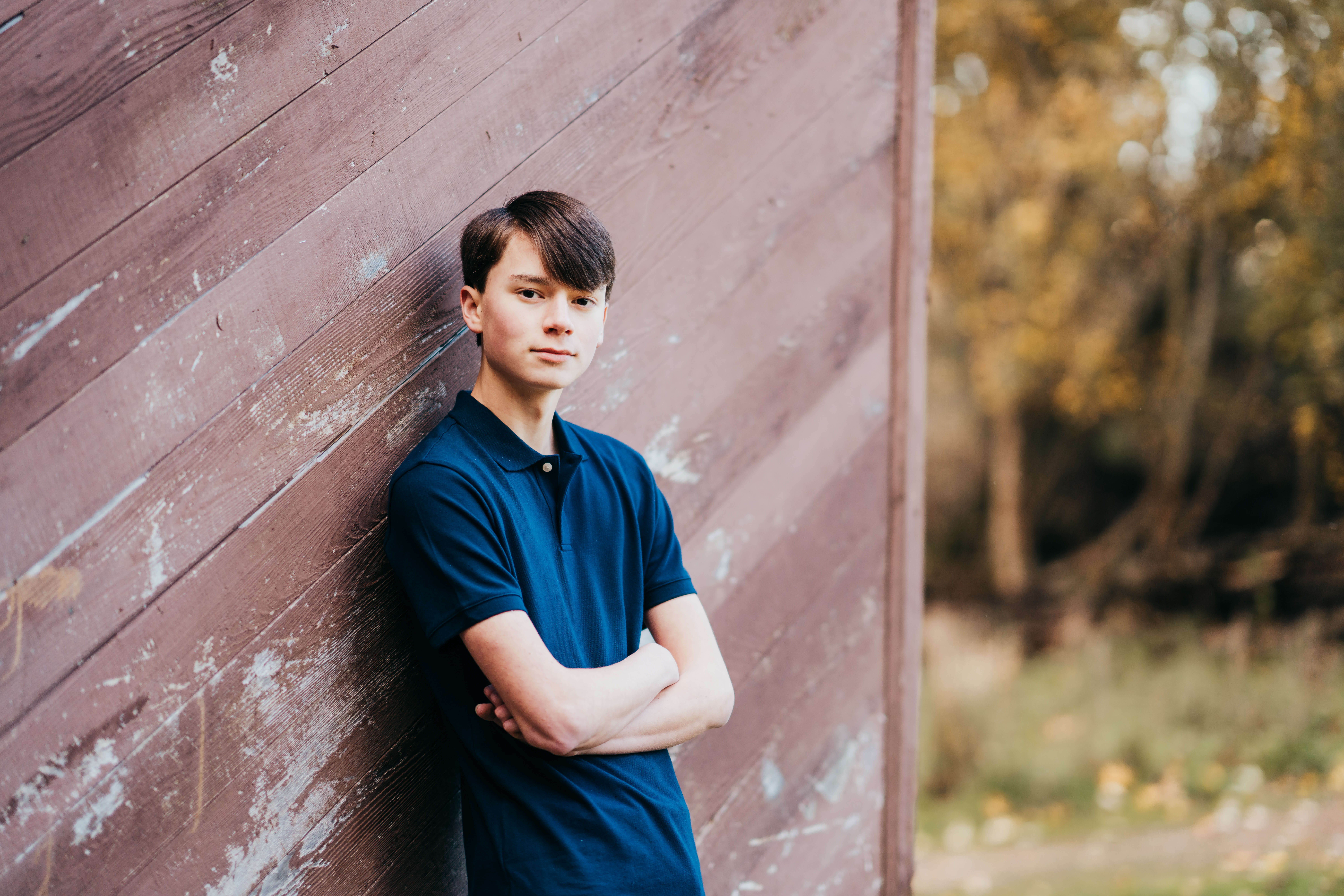 A high school senior leans against a rustic wall in a blue polo with arms crossed after finding High School Internships In Seattle