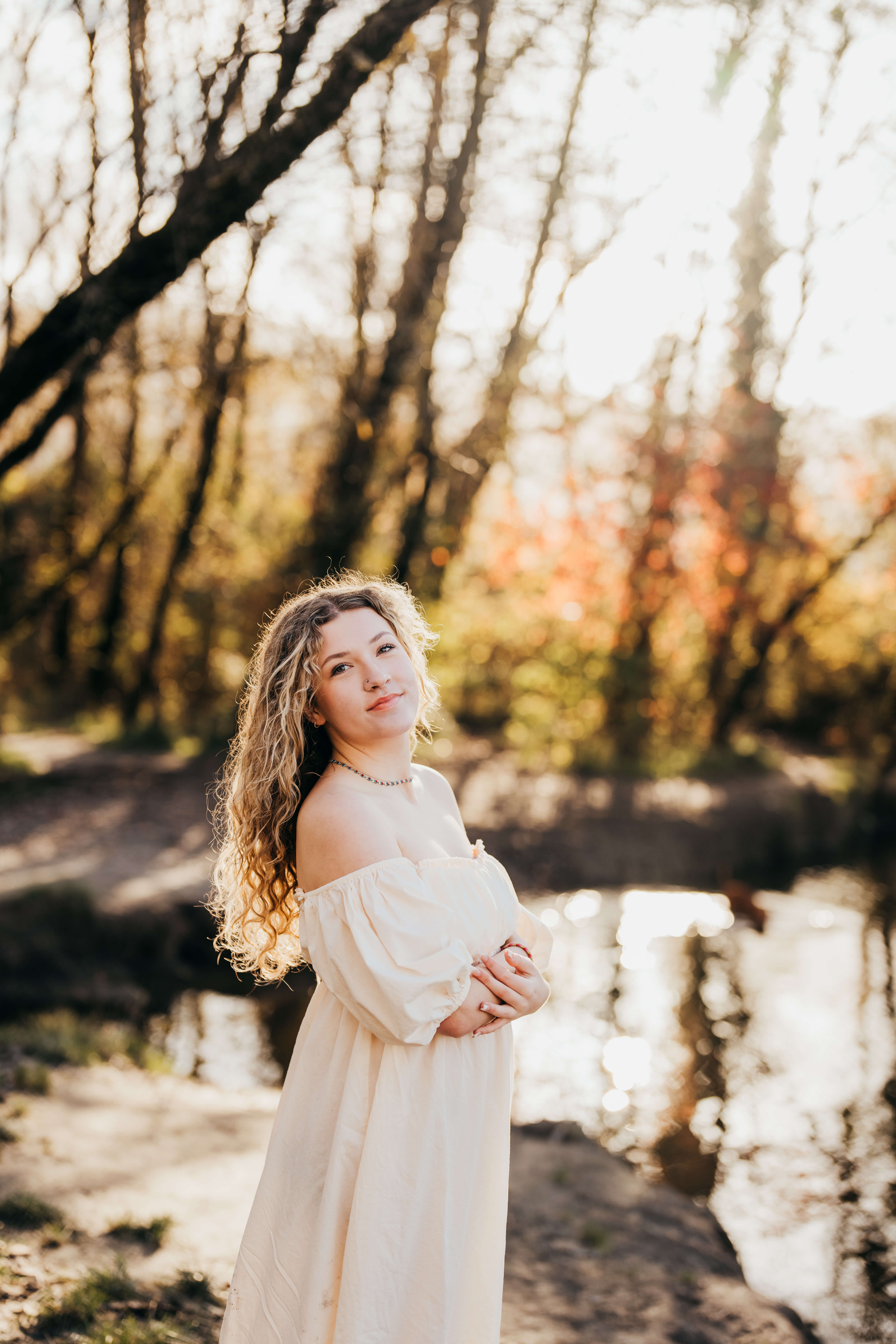 A high school grad walks by a creek at sunset in a white dress after enjoying Running Start Program In Seattle