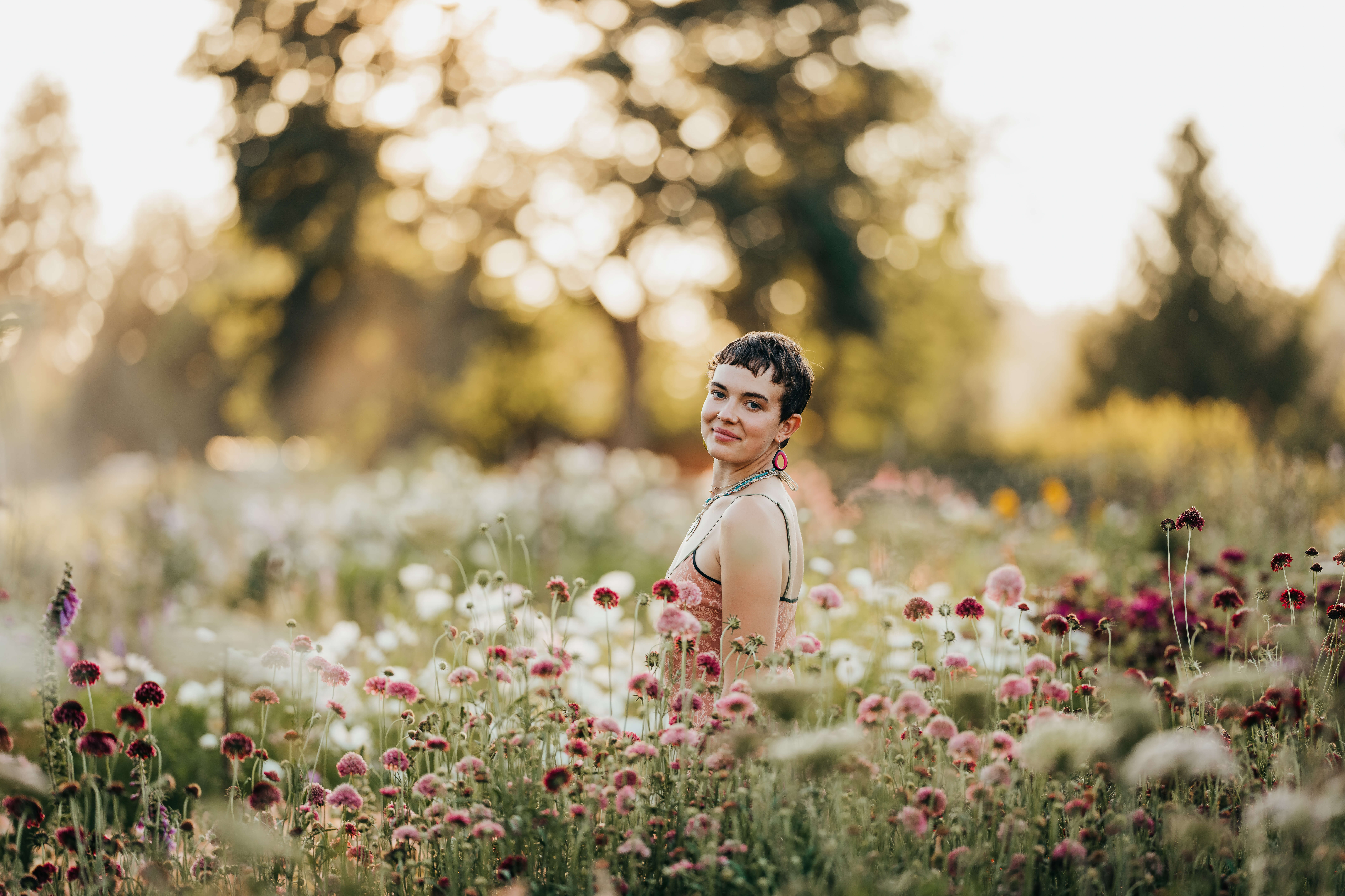 A high school grad in a pink blouse walks in a vibrant flower garden at sunset smiling over their shoulder after enjoying Seattle Promise
