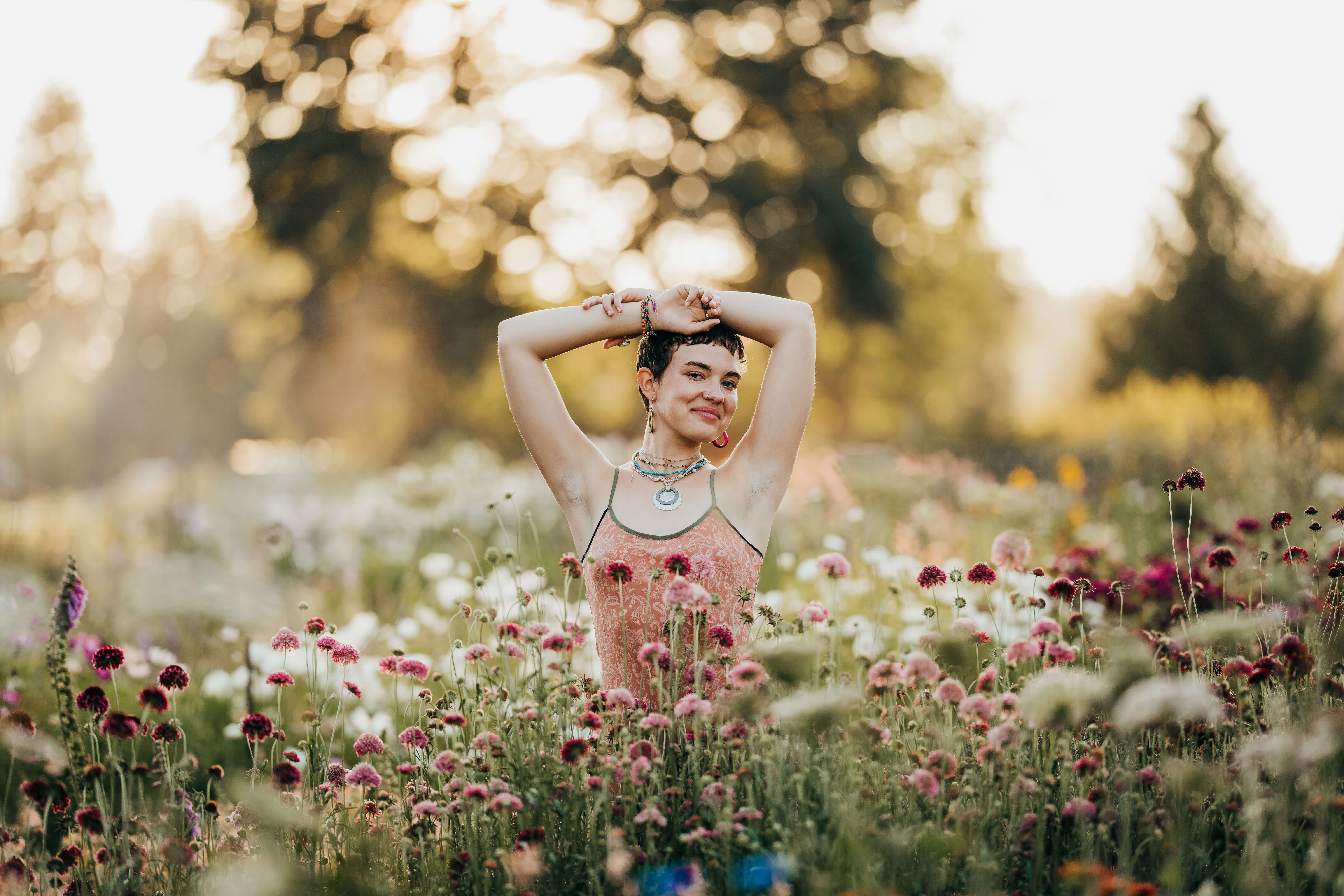 A high school senior stands among colorful flowers in a garden at sunset with arms over their head after using Seattle Promise