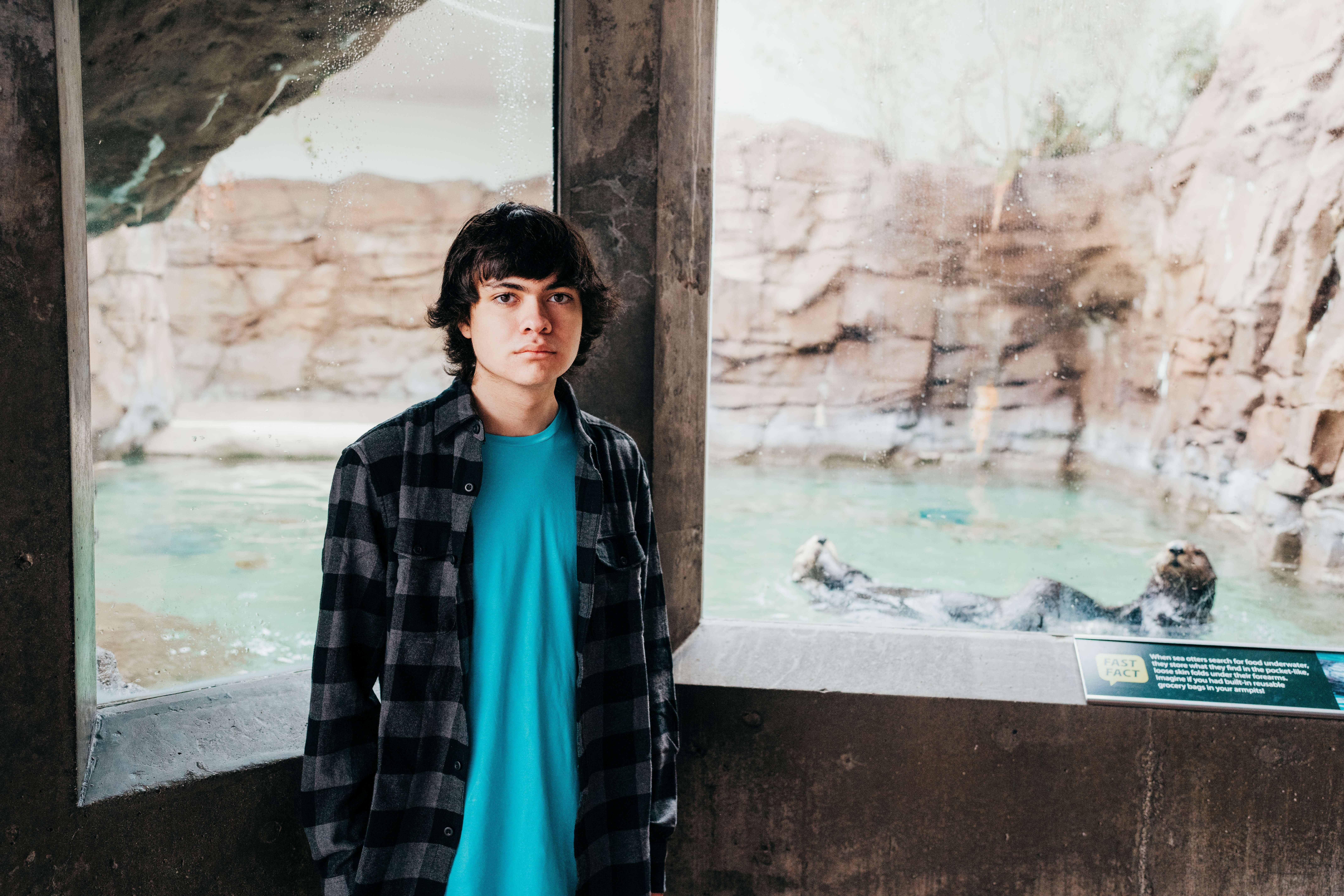 A high school senior stands with an otter at the zoo in a plaid shirt after exploring colleges near seattle