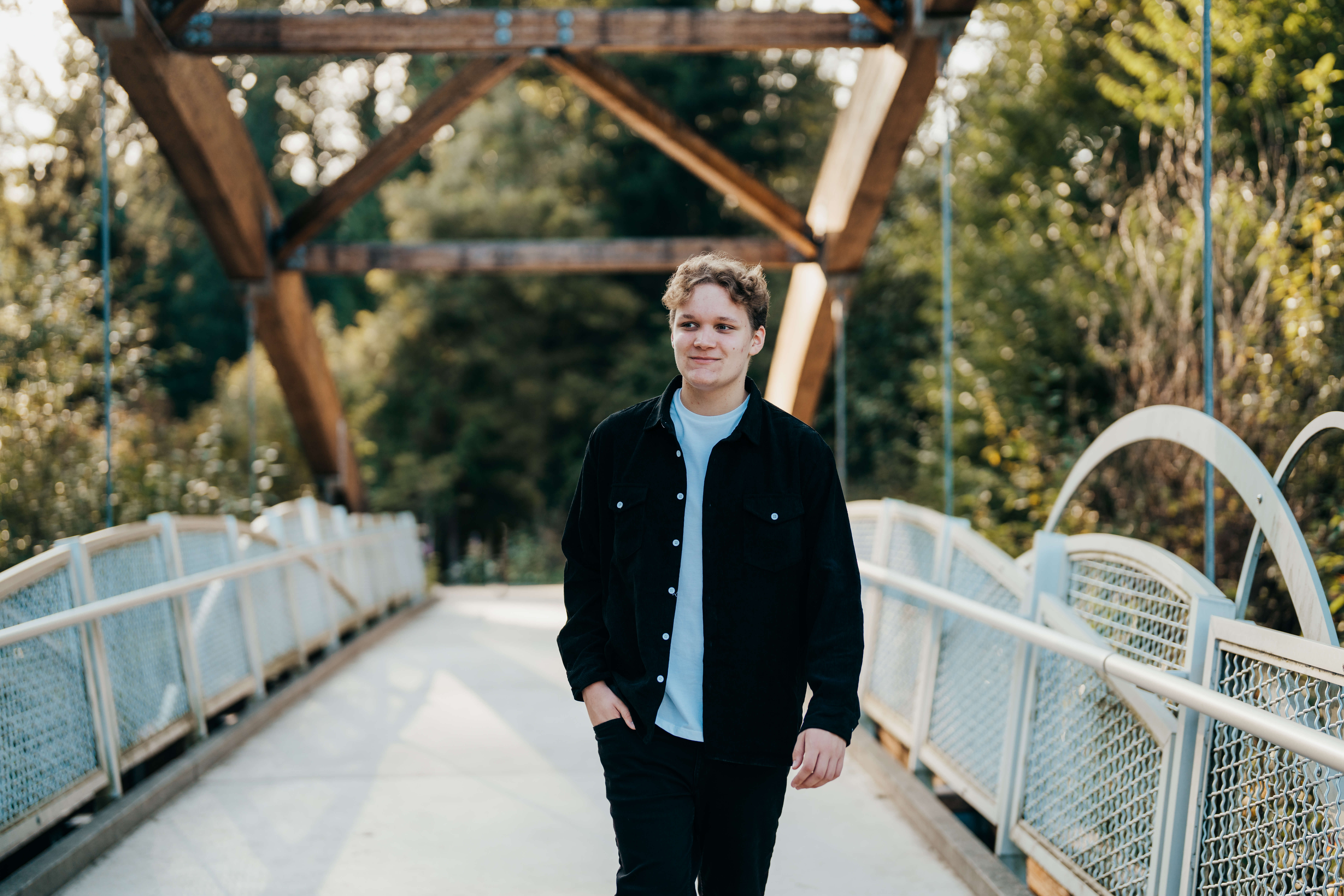 A high school senior in a black jacket walks across a bridge smiling with a hand in his pocket after visiting colleges near seattle