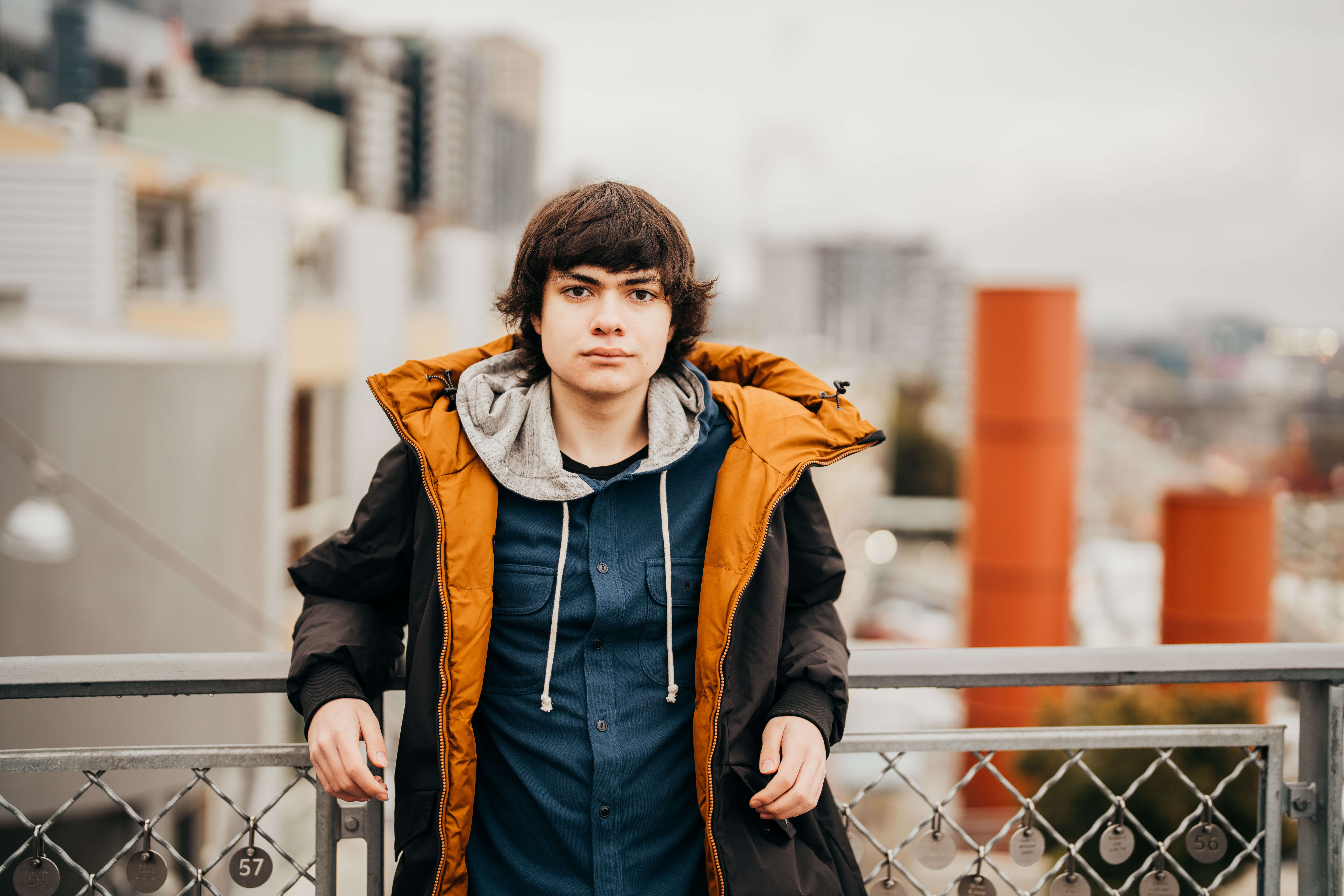 A high school senior in a blue shirt and big dark jacket leans against a bridge railing in downtown Seattle after using cte dual credit