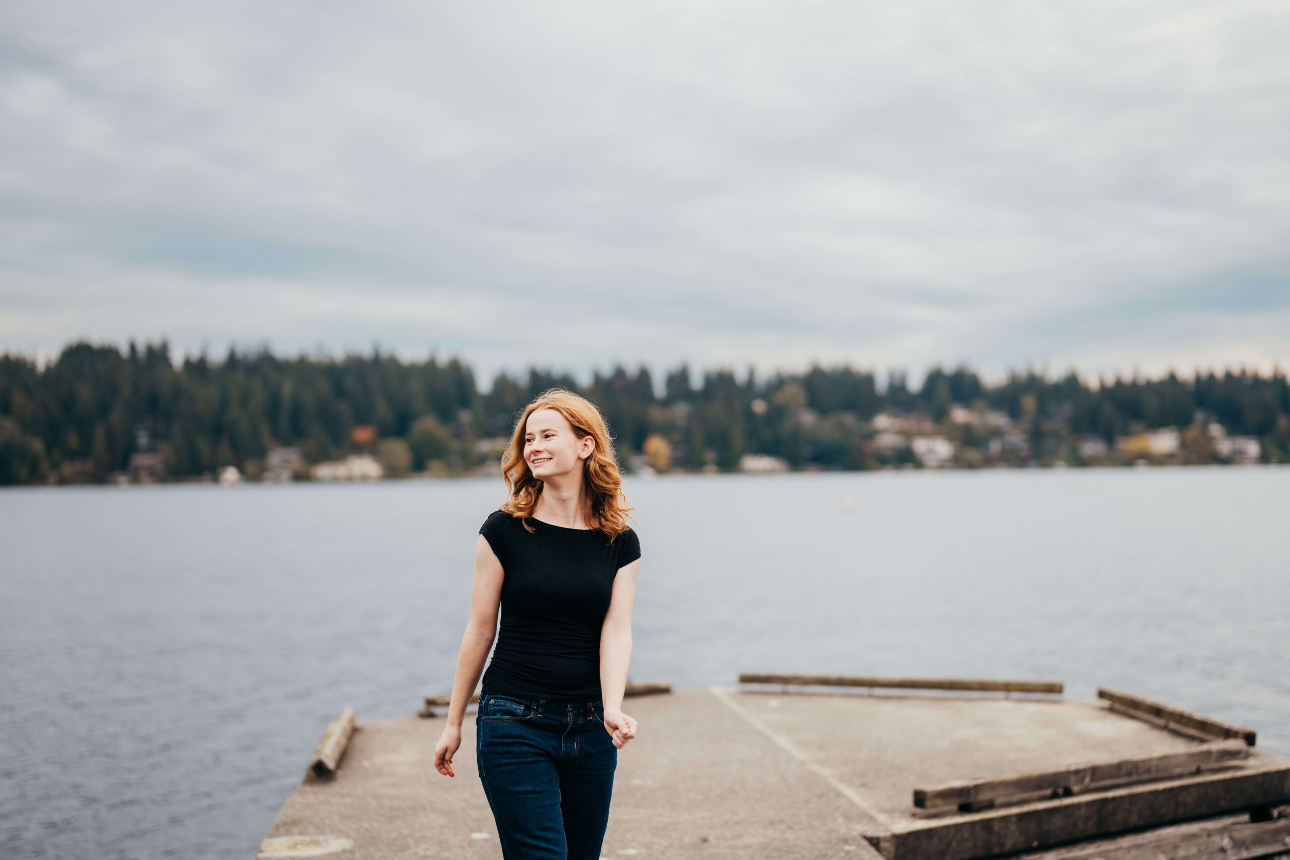 A woman in a black shirt and red hair walks on a dock smiling over her shoulder after visiting hair salons in seattle