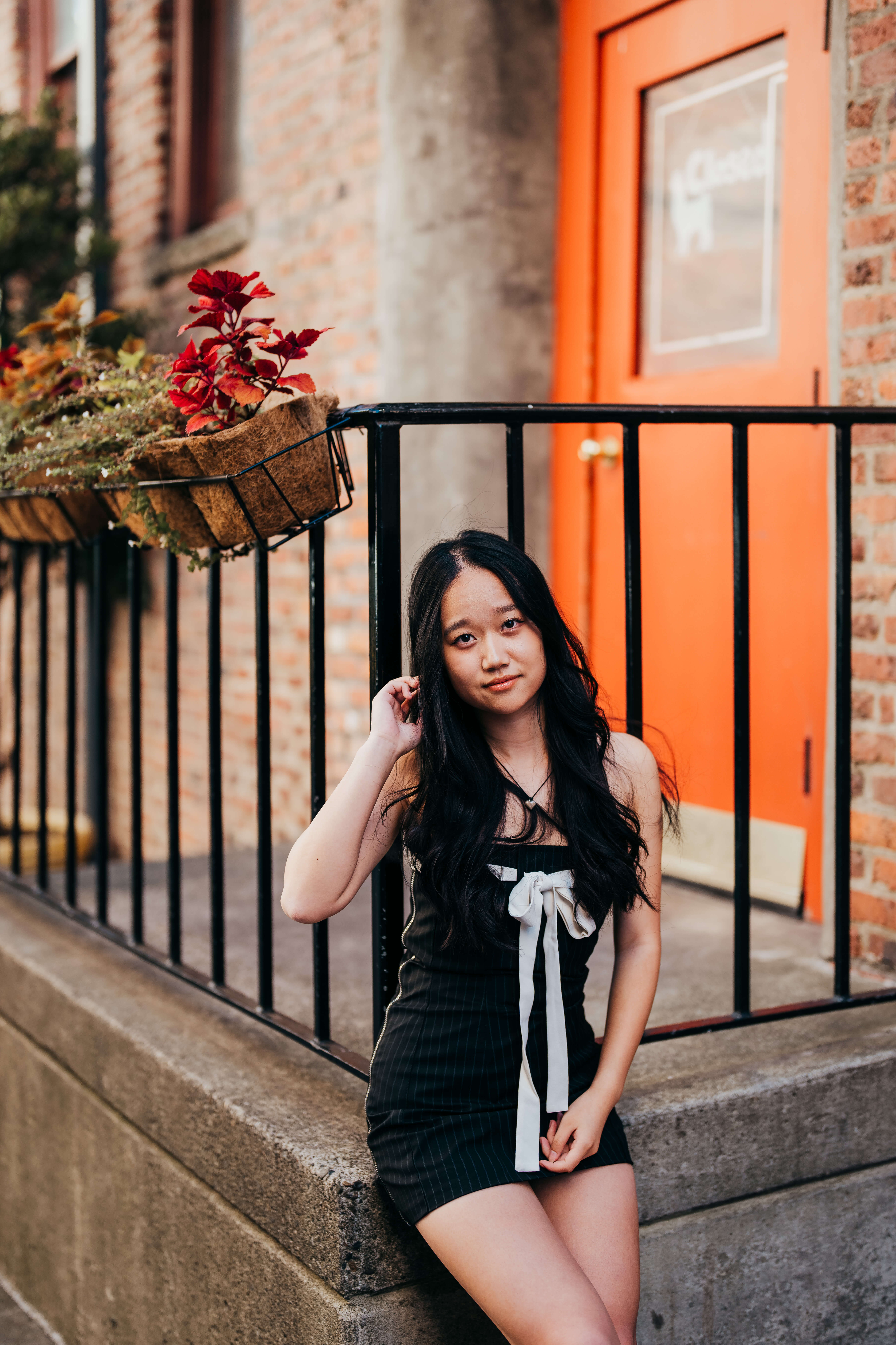 A high school senior in a black dress with white bow in front leans against a railing under flowers after finding scholarships in seattle
