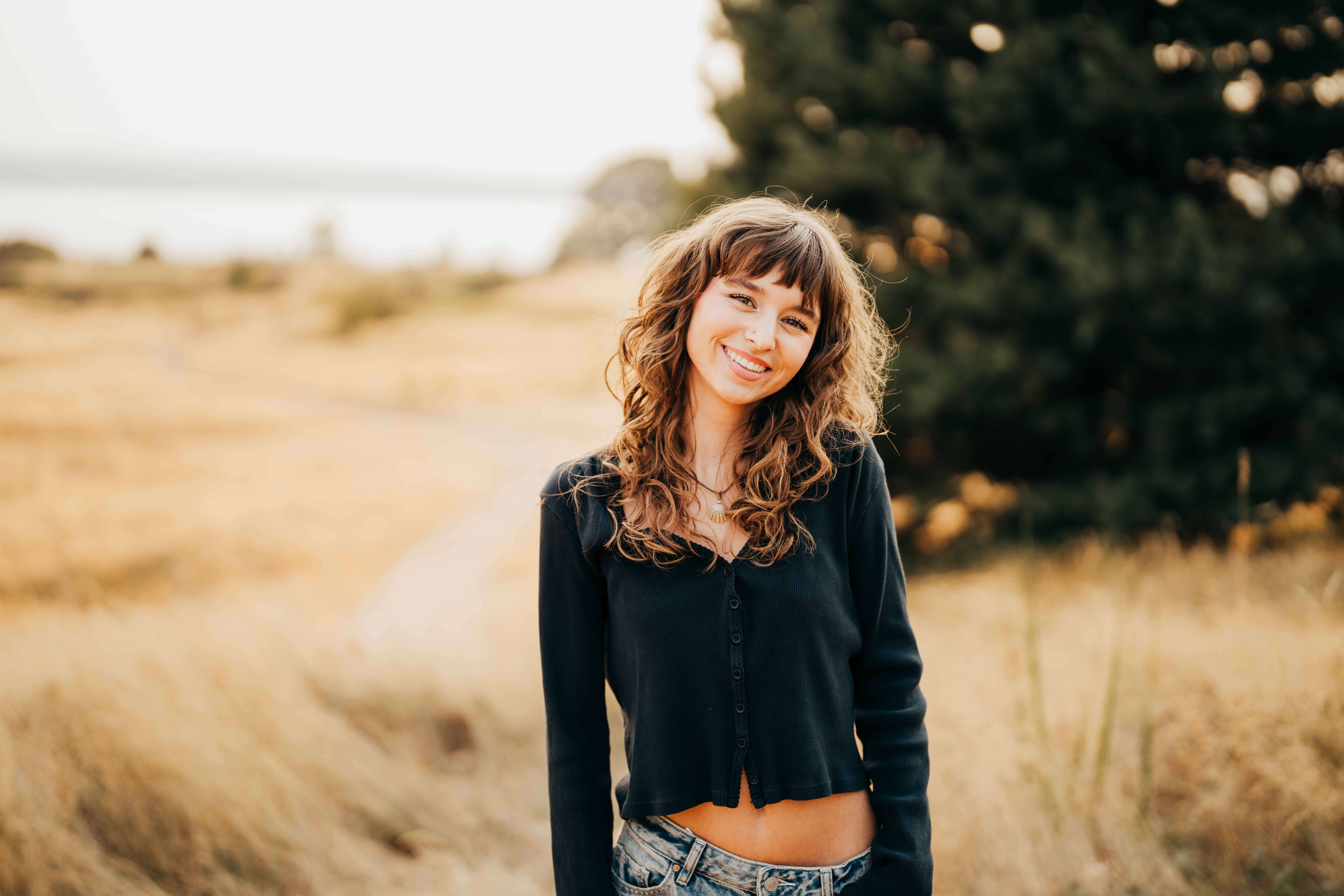 A high school senior in a black shirt smiles while on a hike in tall golden grass after serving as a volunteer on mercer island