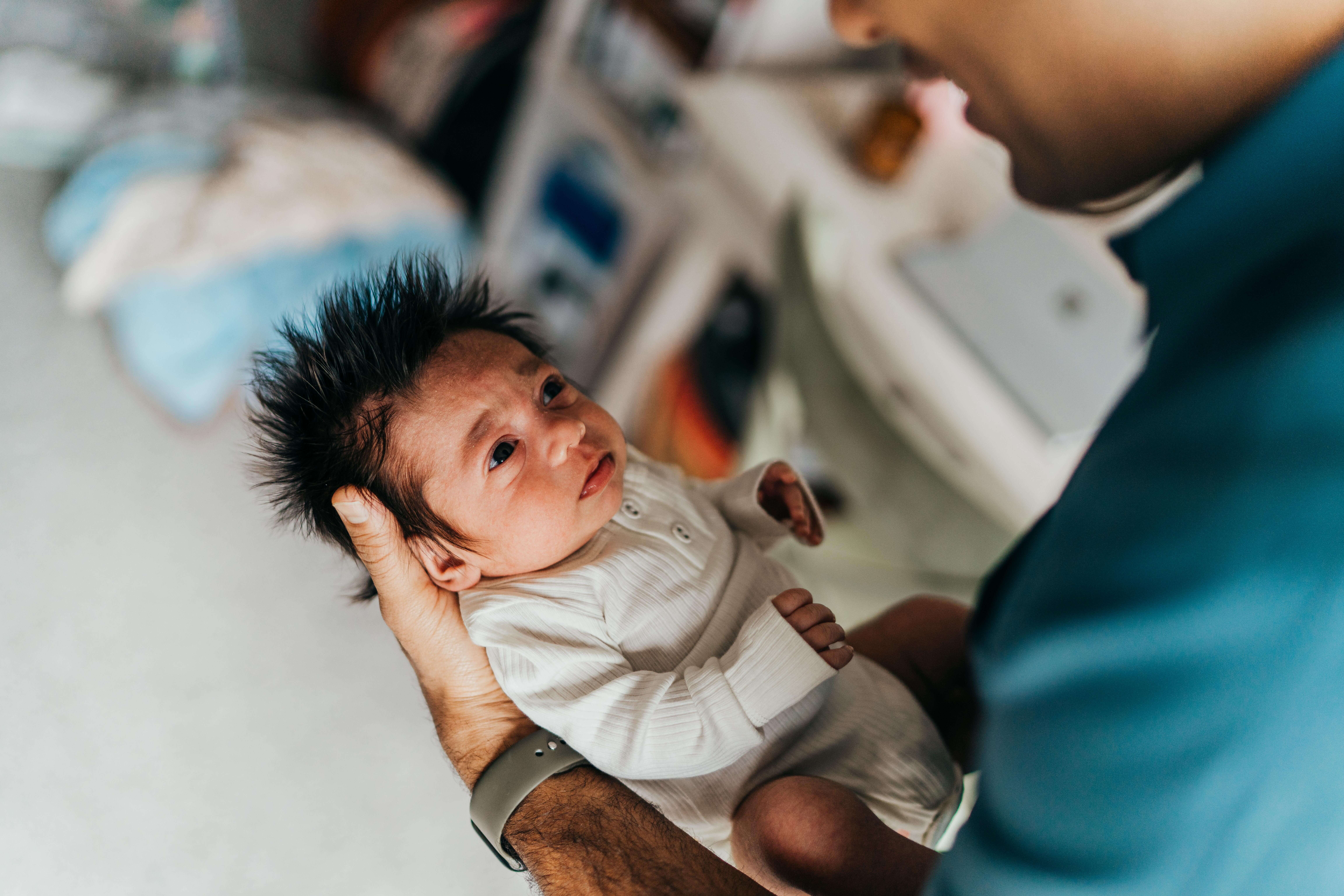 A newborn abby in a white onesie lays in dad's hands looking up to him before finding a frenectomy in seattle