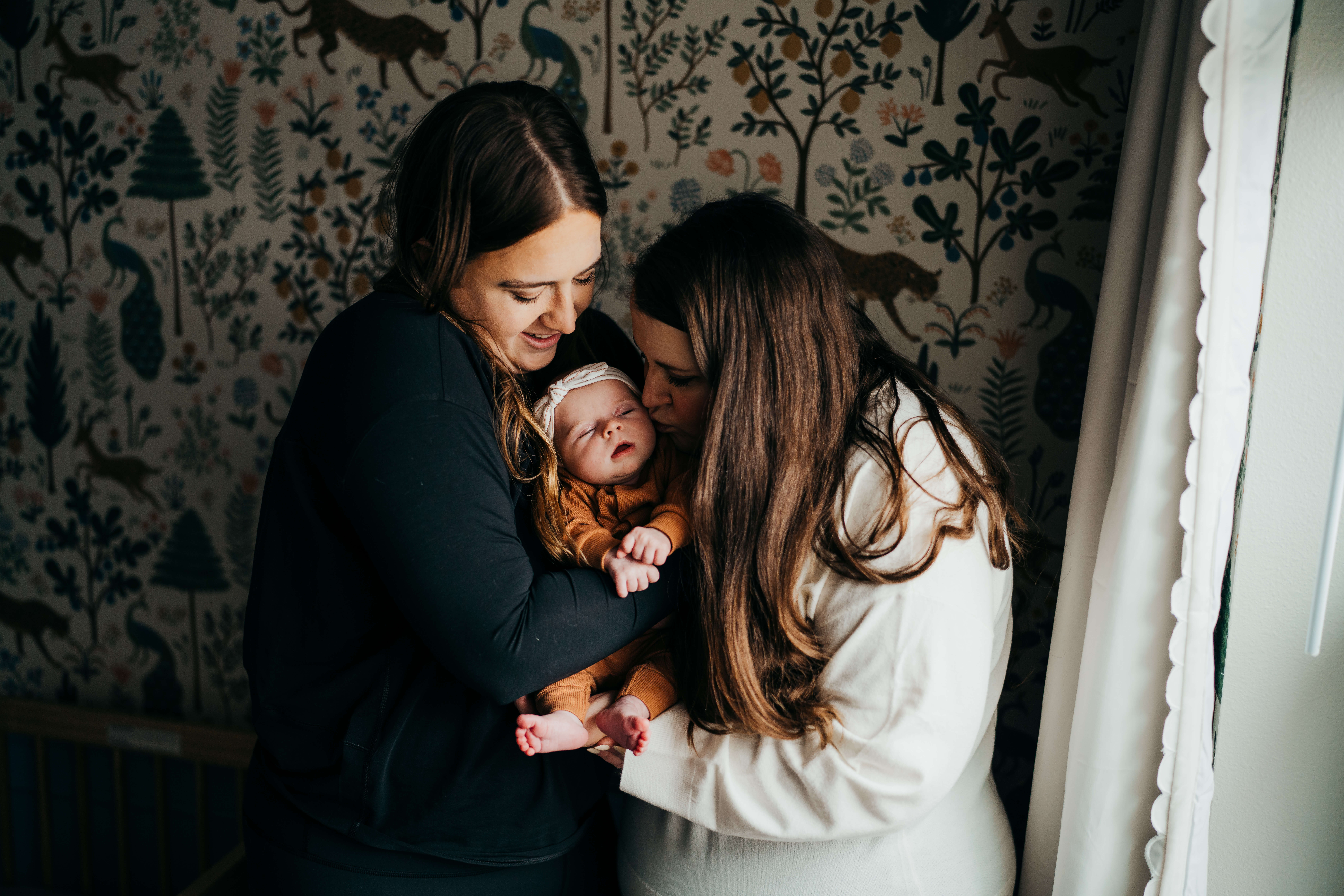 New mom in black and white sweaters cradle and kiss their sleeping newborn daughter