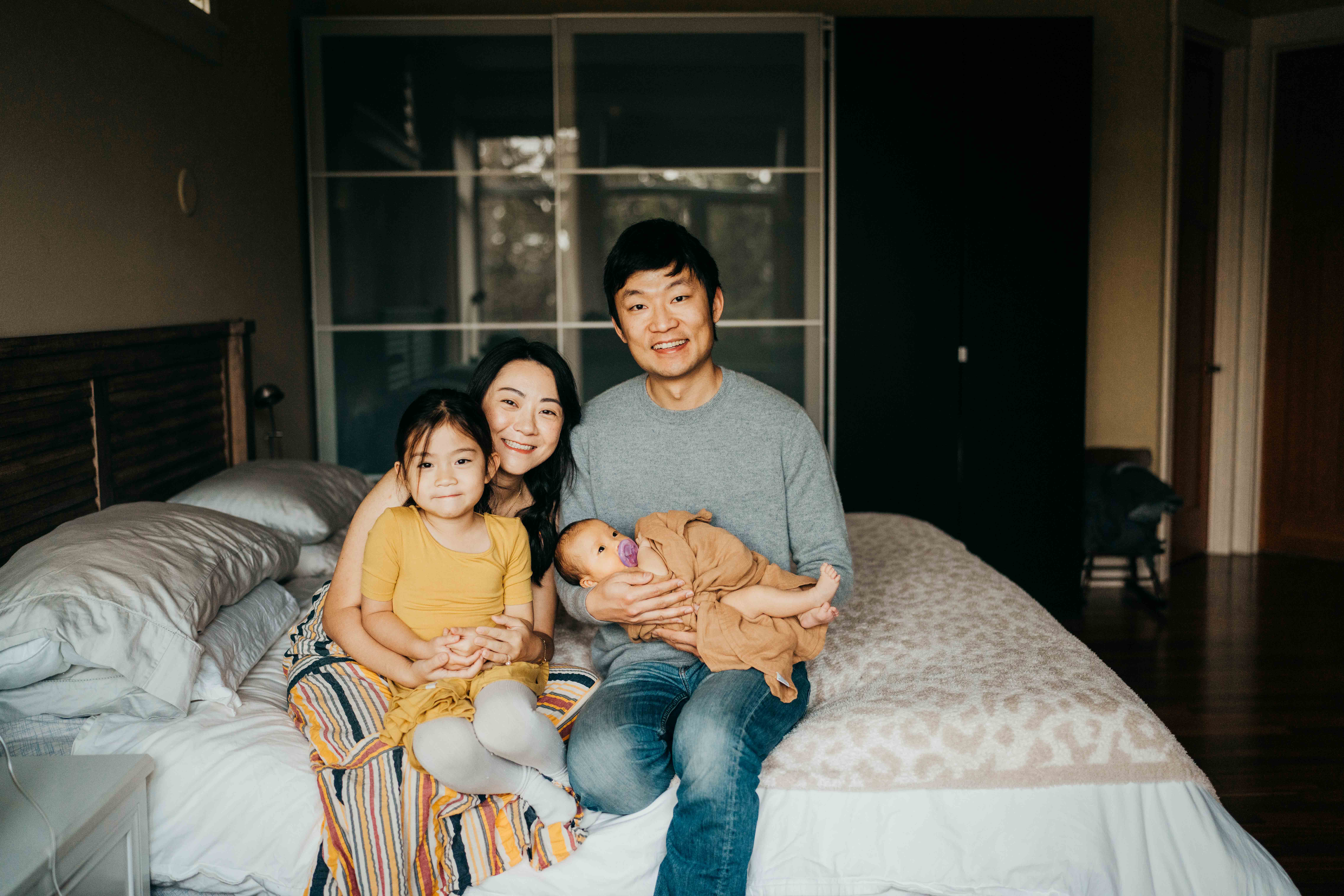 Happy mom and dad sit on a bed with their newborn and toddler daughter in their laps thanks to support from peps seattle