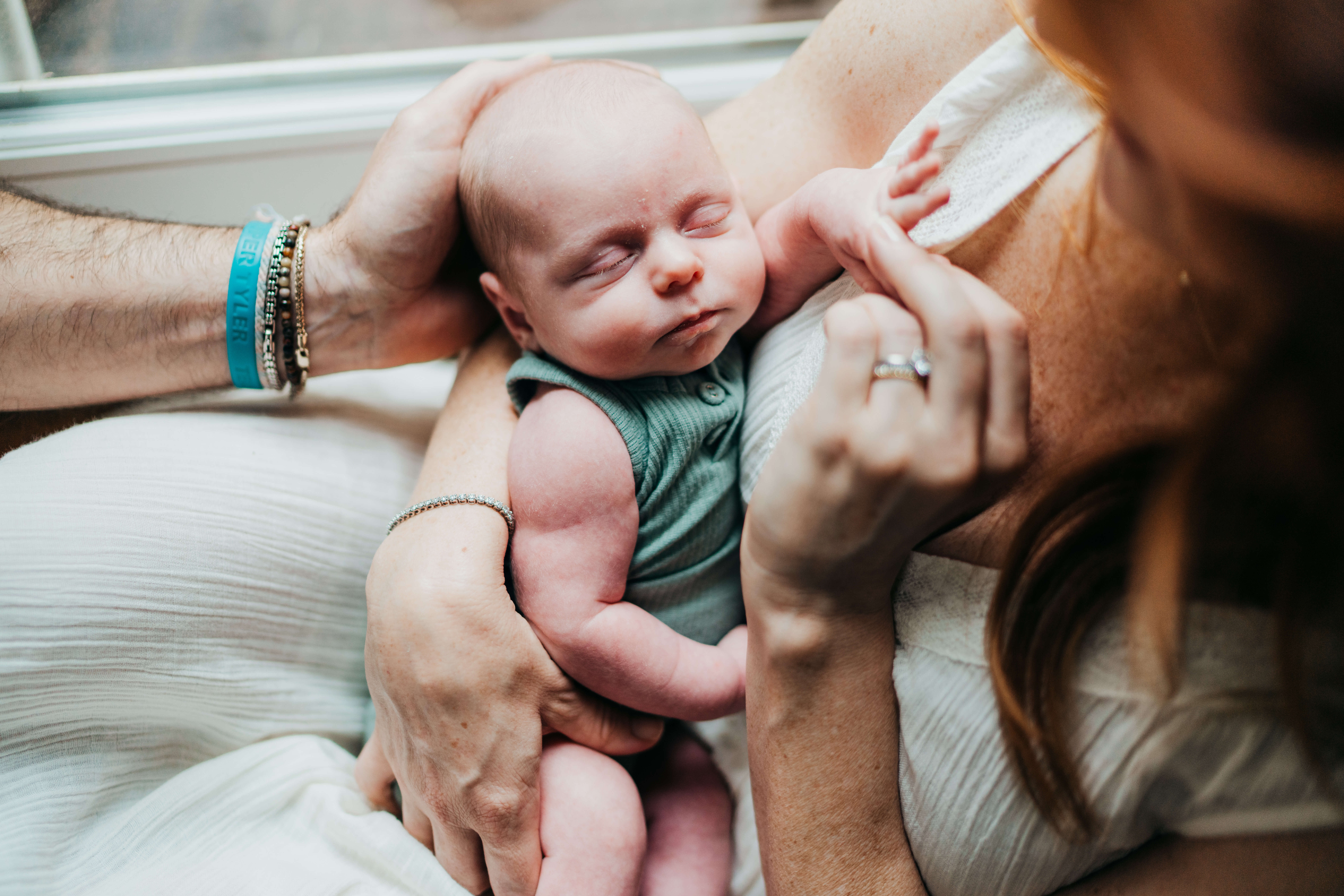 A newborn baby sleeps against mom's chest in a green onesie