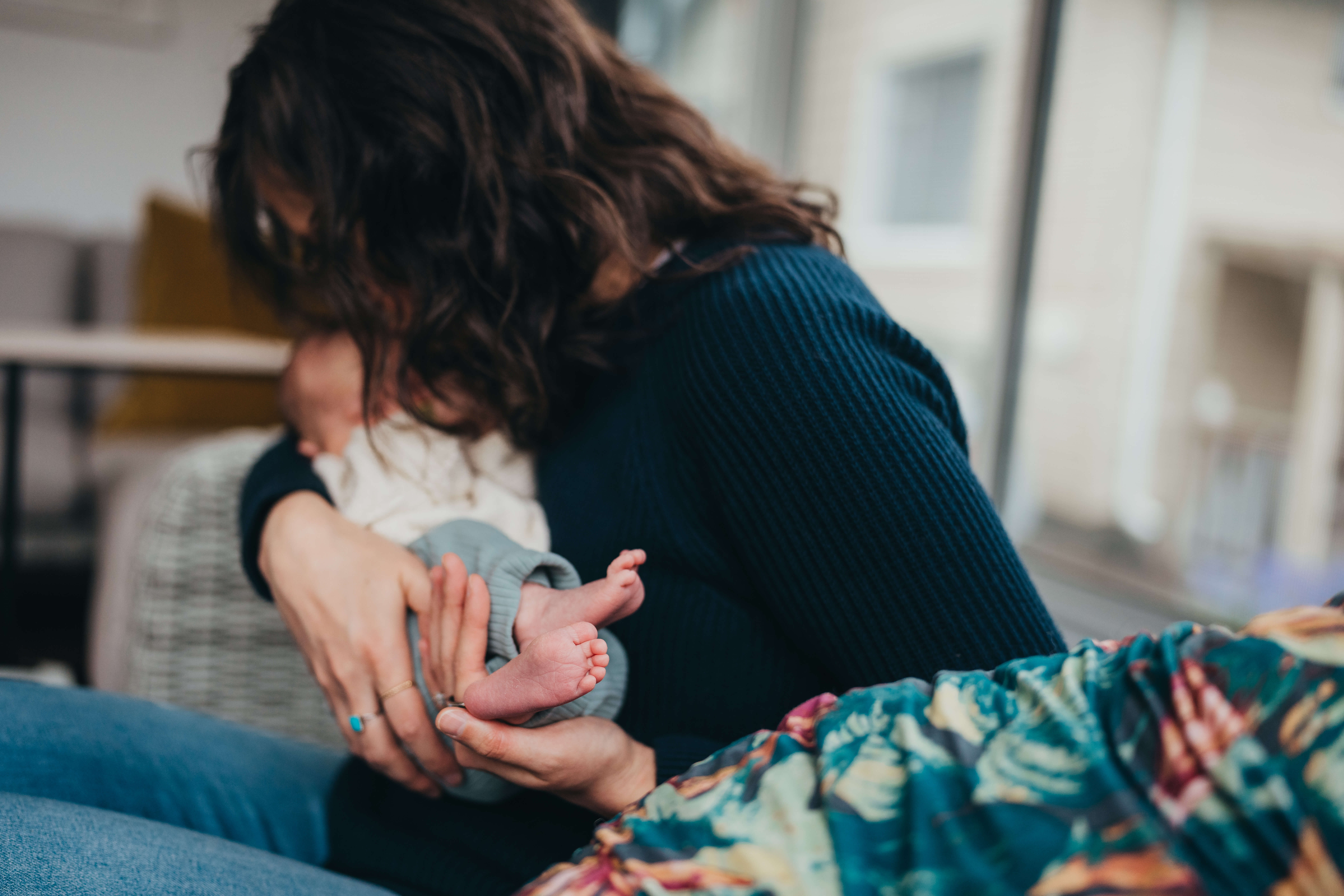 A happy mother kisses her sleeping newborn while cradling her feet on a couch