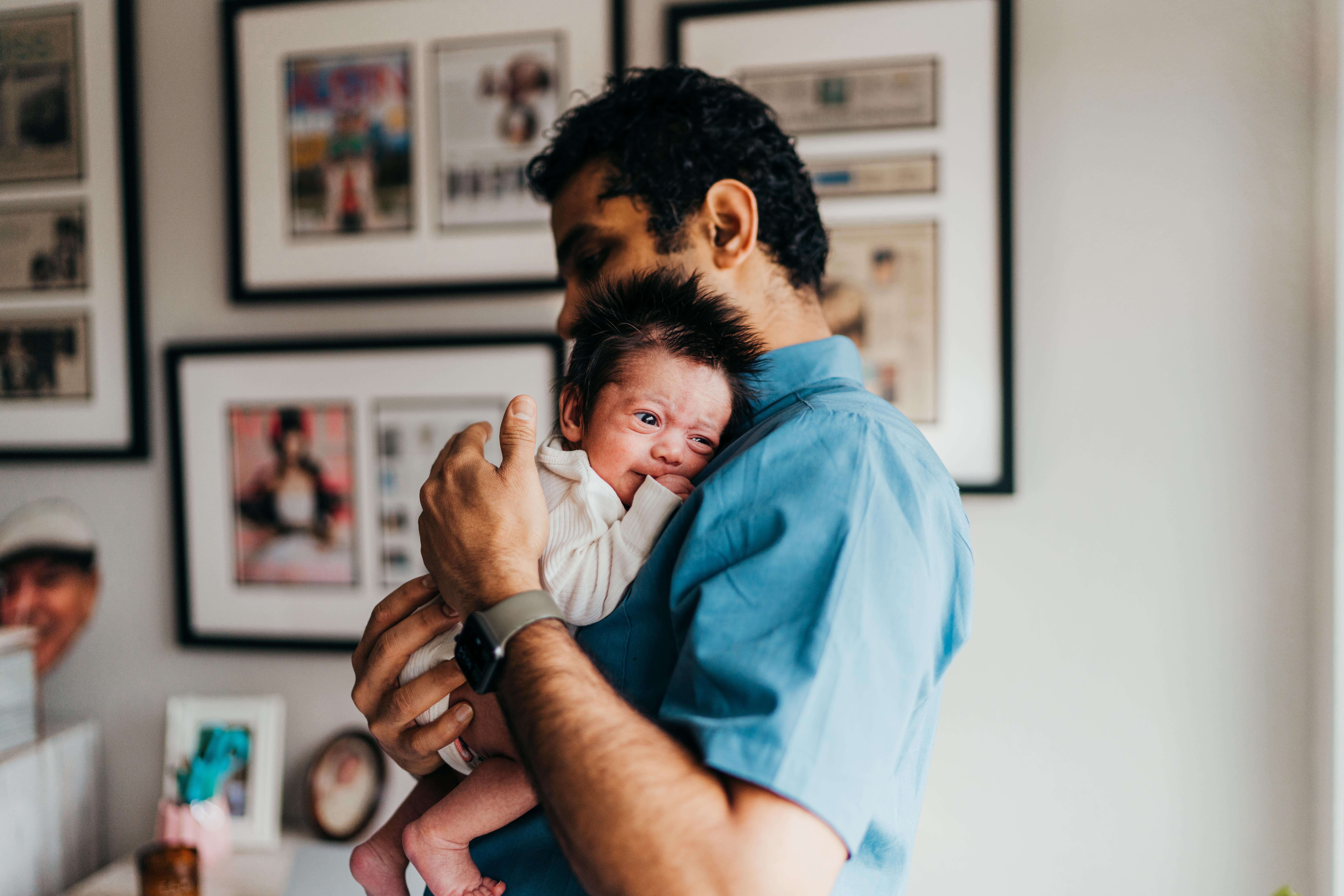 A new dad cradles his newborn baby against his shoulder while standing in a nursery after visiting two owls seattle